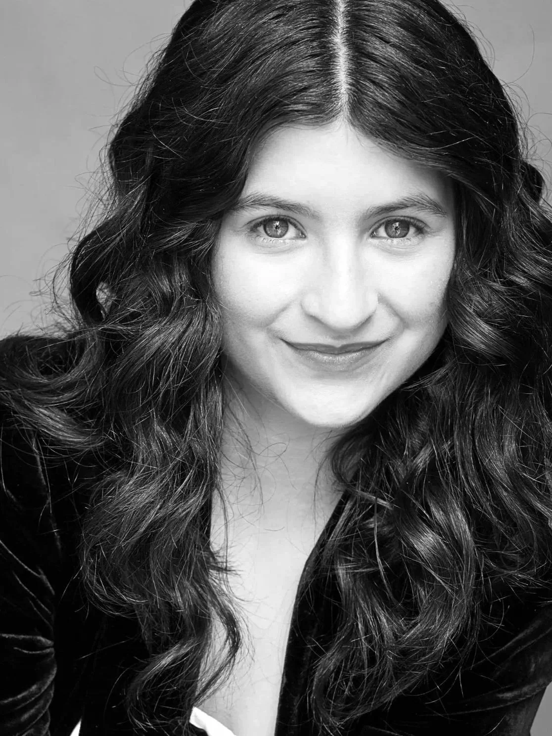 Black and white portrait of a woman with wavy, long hair, smiling, wearing a dark top.