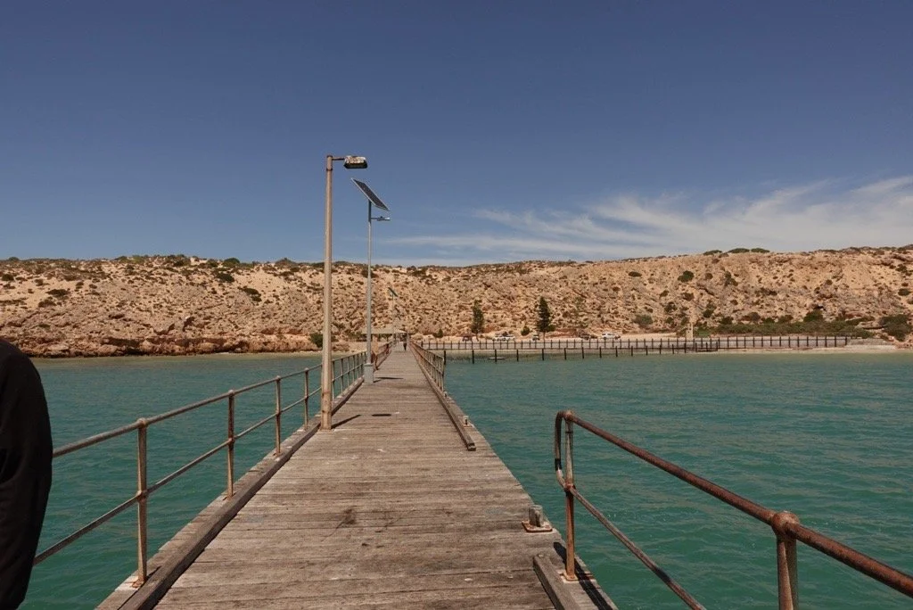 A scenic landscape of a jetty with sandhills in the background