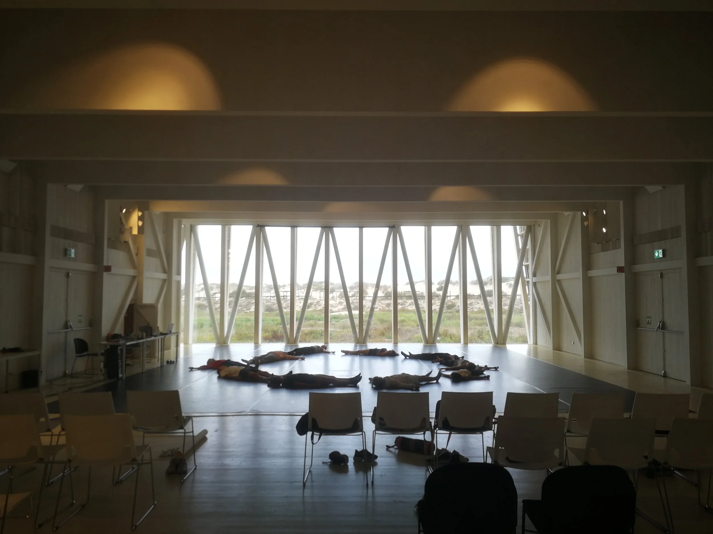 People lying on the floor in a large, bright room with an open view of the outdoors through floor-to-ceiling windows.