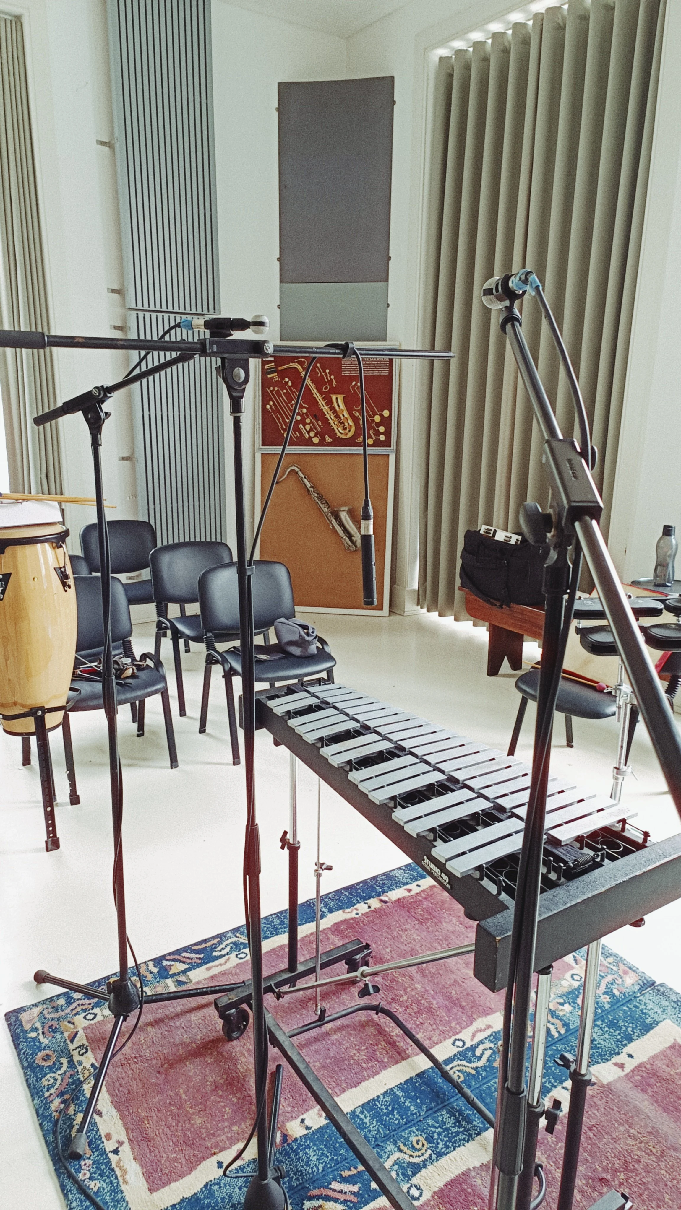Musical studio with microphones, chairs, and musical instruments including a vibraphone, all set up for recording or rehearsal.