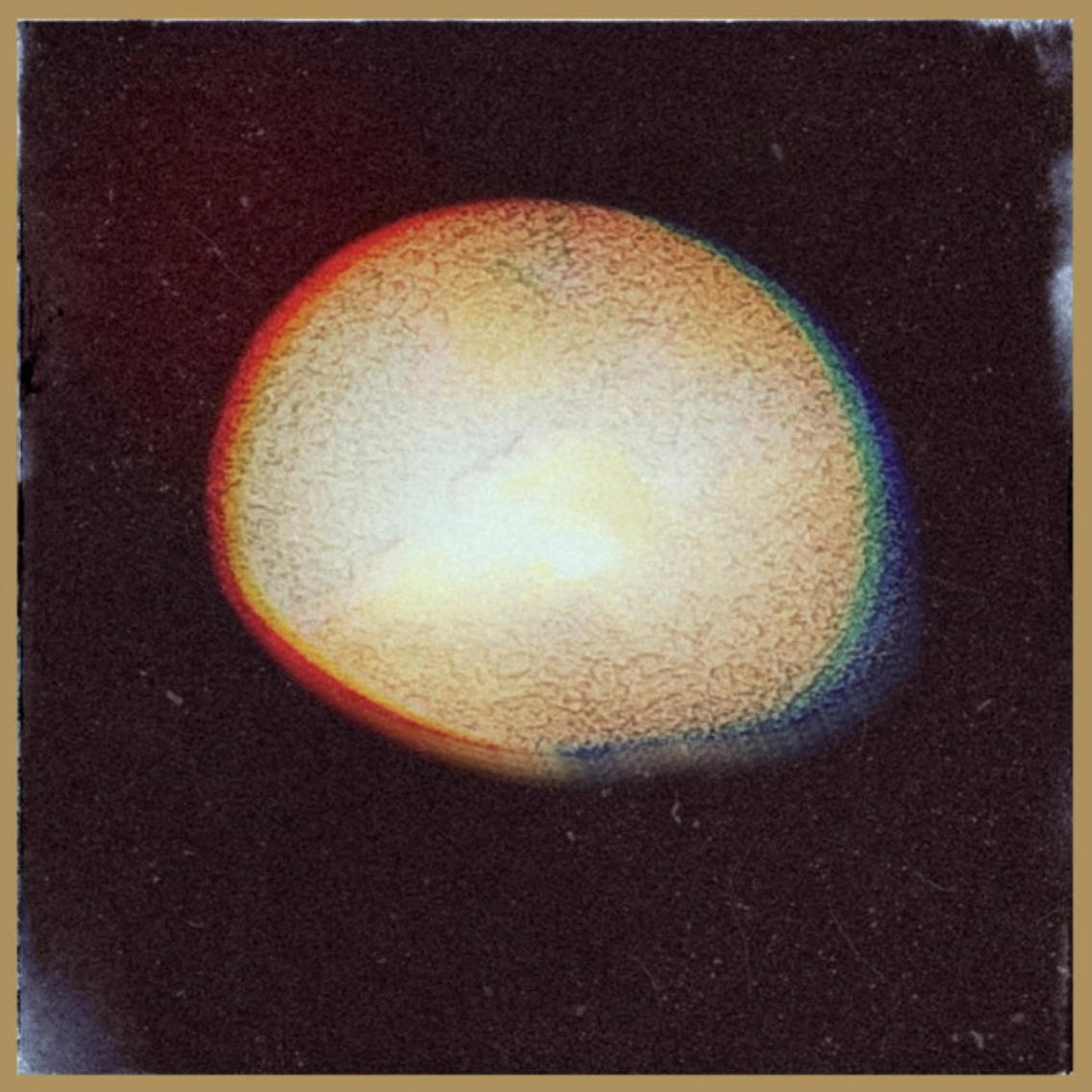 A bright, glowing spherical object with a yellow center and a multicolored halo against a dark background.