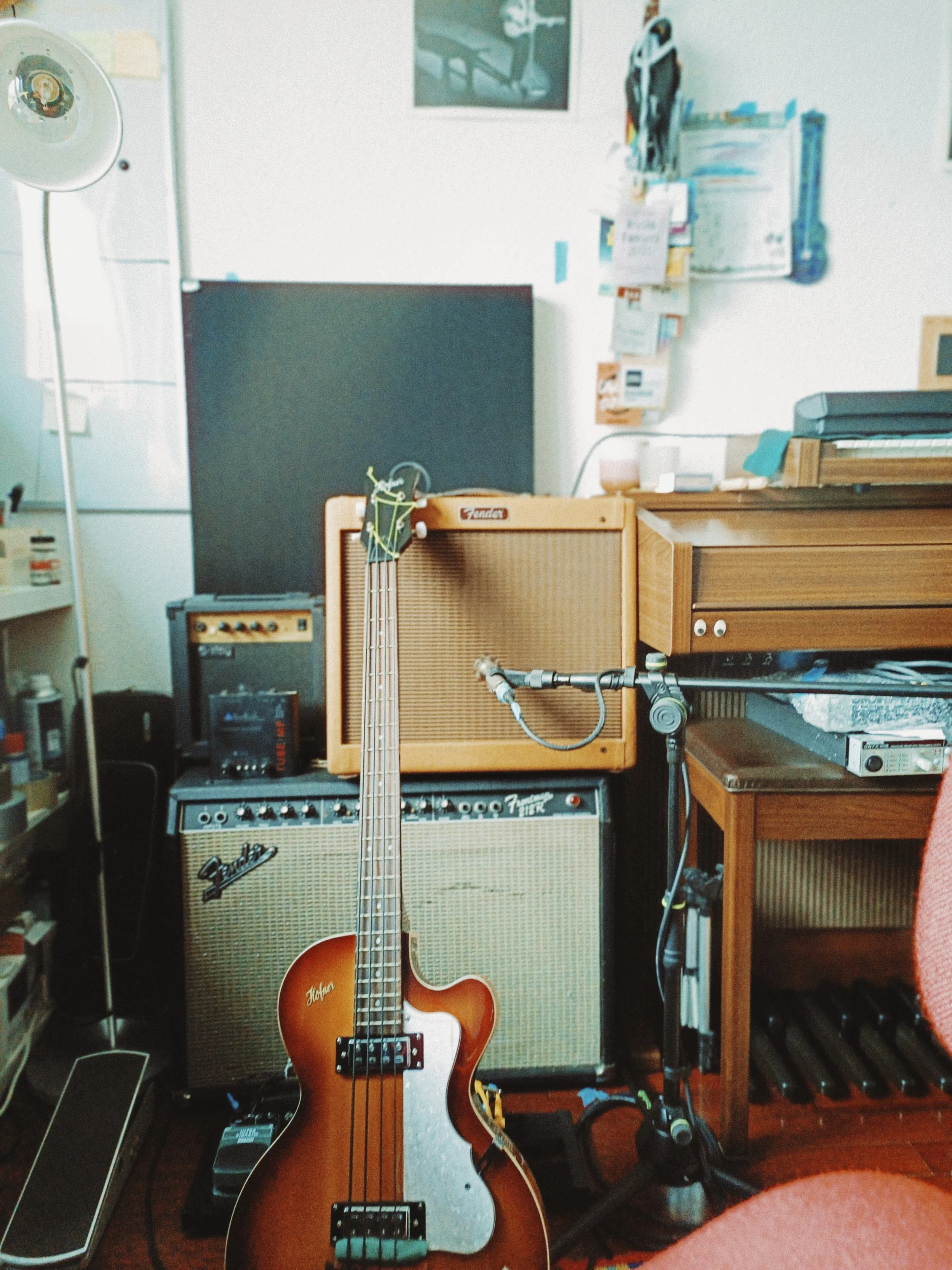 A room with musical equipment including a Fender guitar, guitar amplifiers, a microphone, and a music stand, with shelves and various items on the walls.