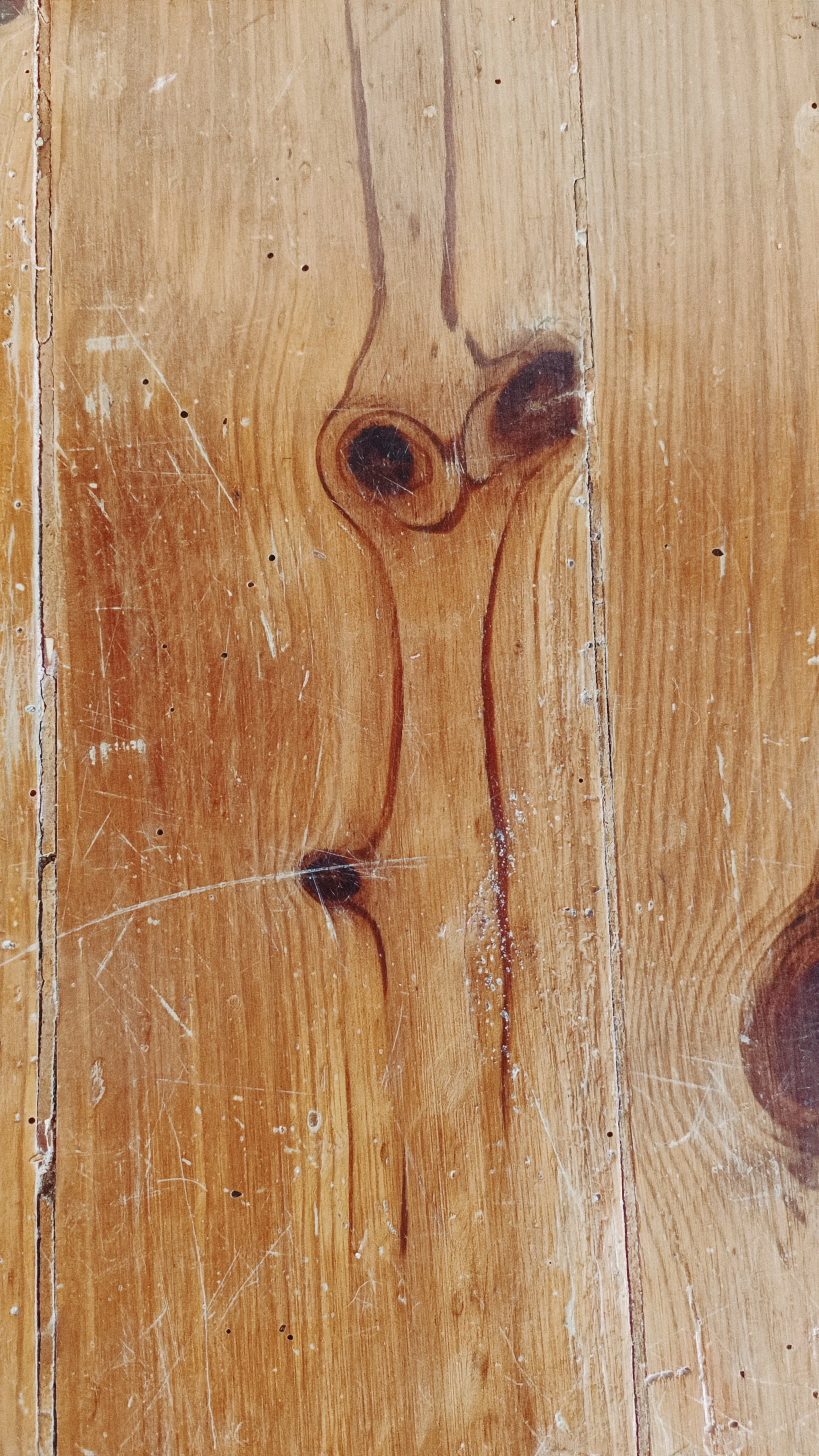 Close-up of a wooden surface with a hand-drawn sketch of a nose and face. The wood has visible grain, knots, and some scratches.