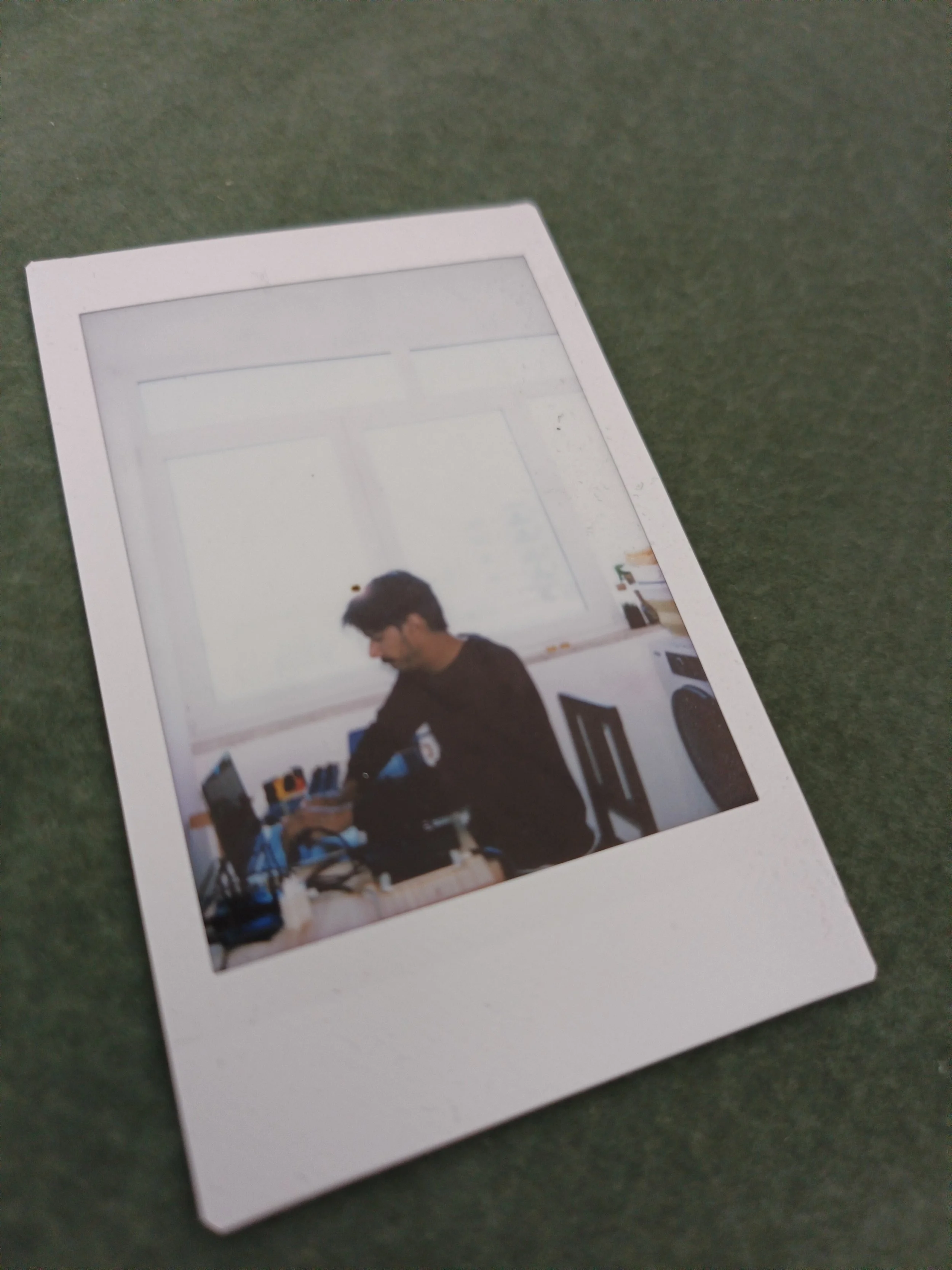 A printed photograph of a person working at a desk with computer equipment, placed on a green surface.