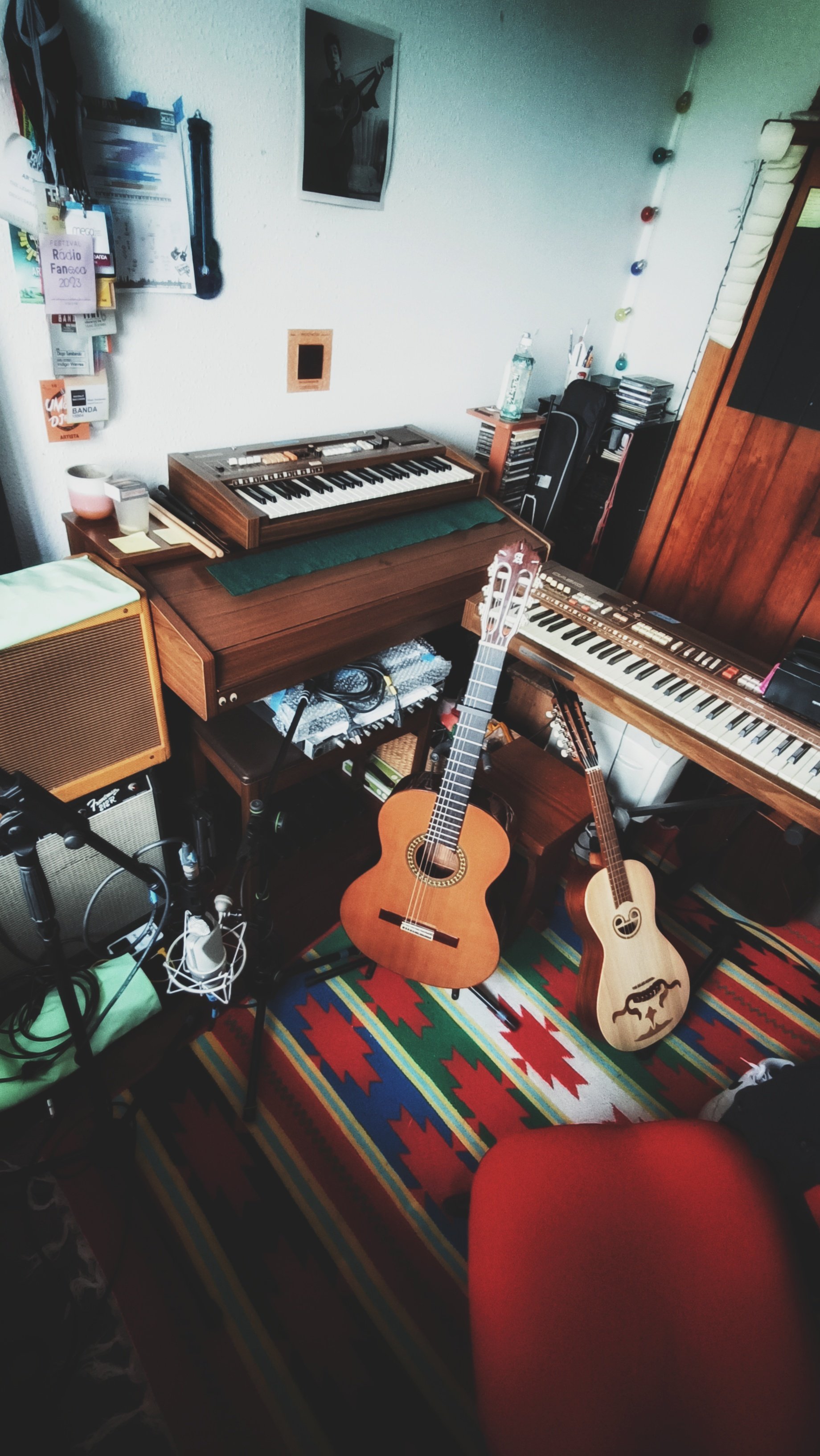 A music studio with two guitars, a keyboard, a mixer, a colorful rug, and various music equipment and decorations.