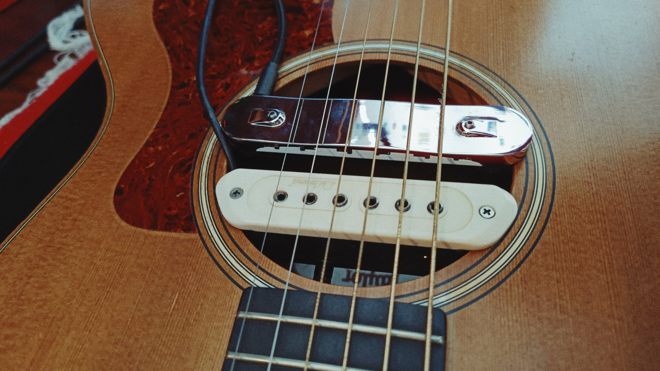 Close-up of an acoustic guitar's sound hole with a white single-coil pickup and six strings.