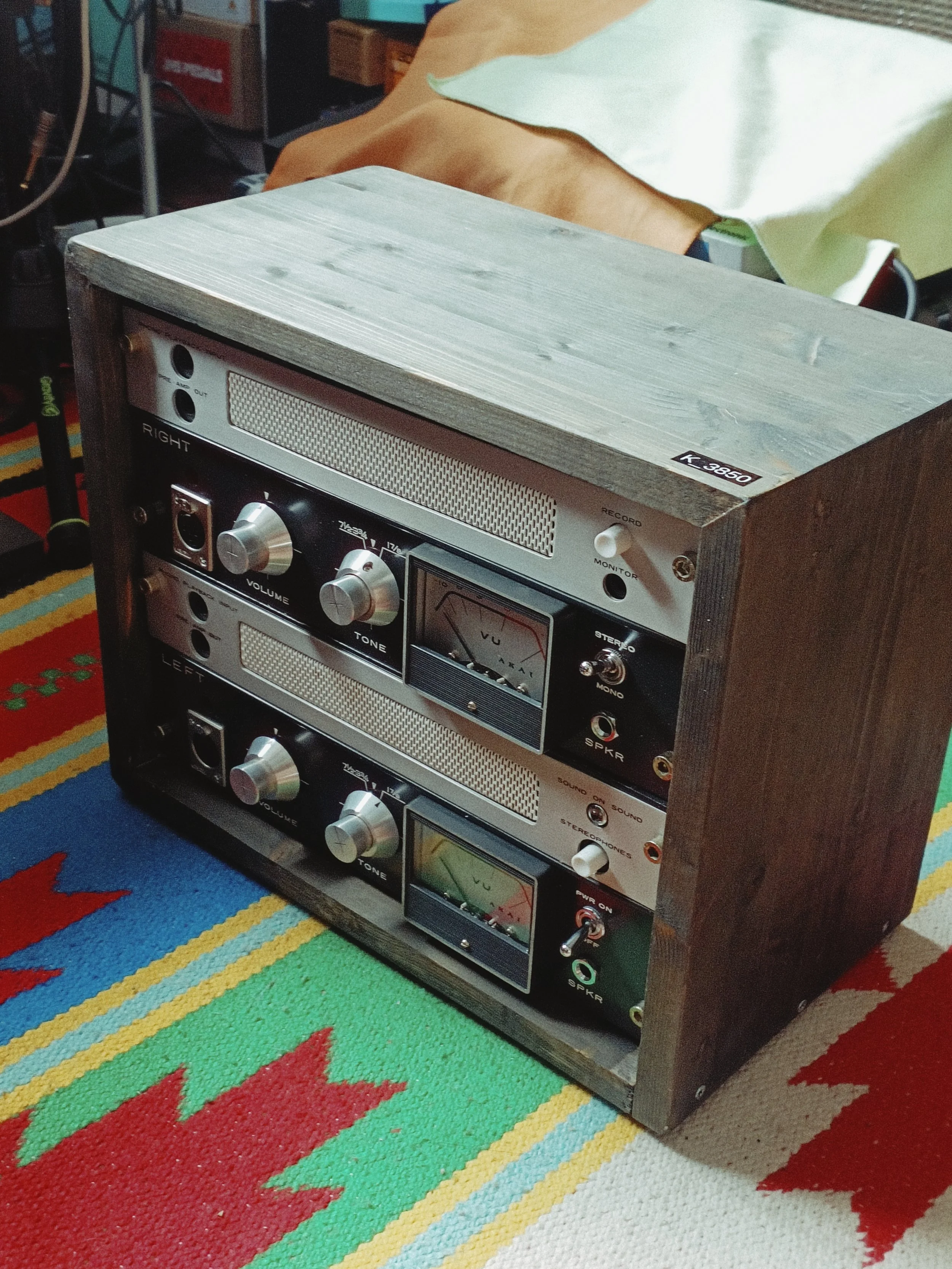 A vintage stereo system with wooden sides and silver front panels, placed on a colorful striped rug with red stars, in a room with various household items in the background.
