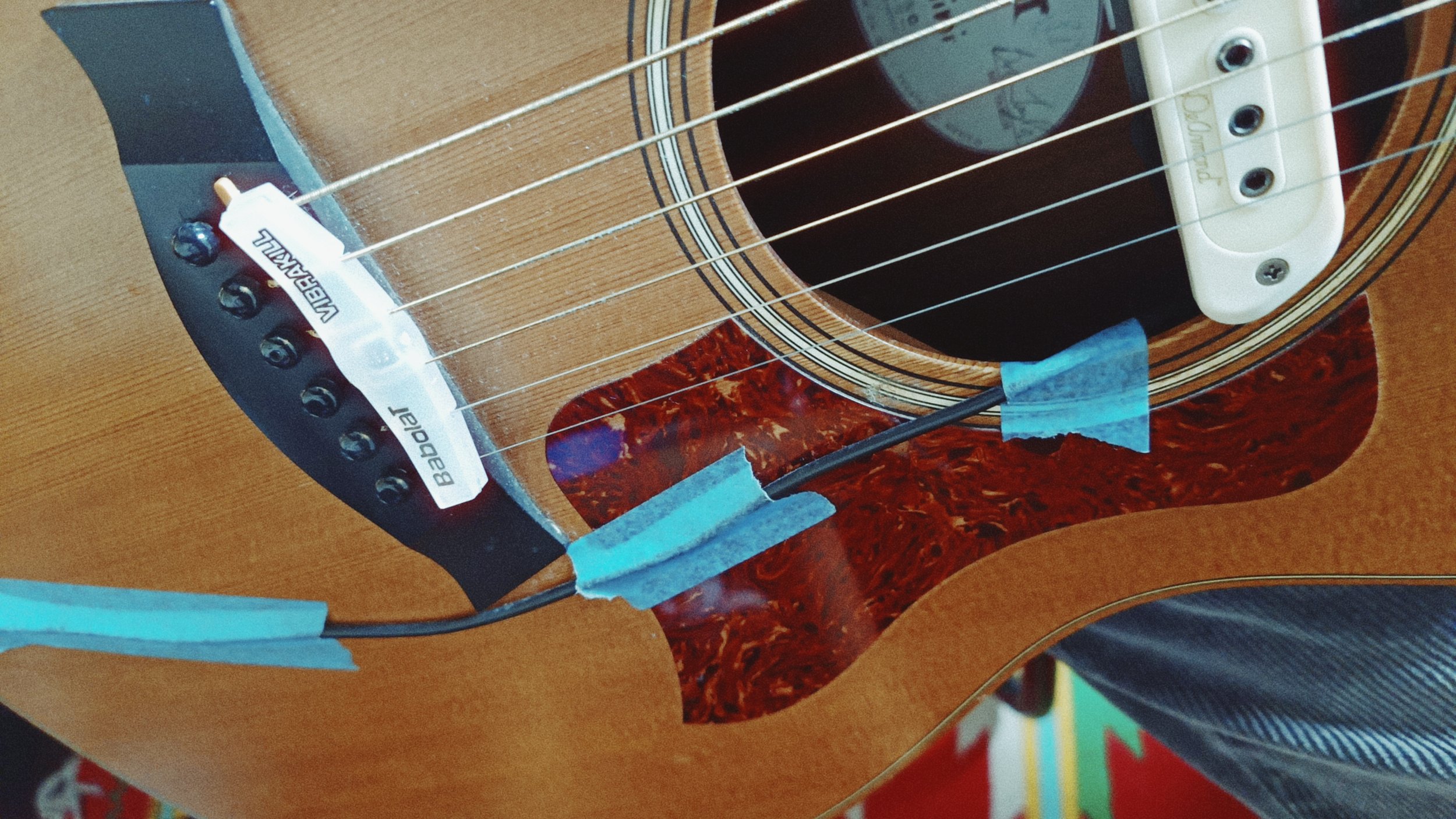 Close-up of an acoustic guitar's body with a focus on the bridge, strings, and pickguard, showing a Carl's Boodal sticker on the bridge.