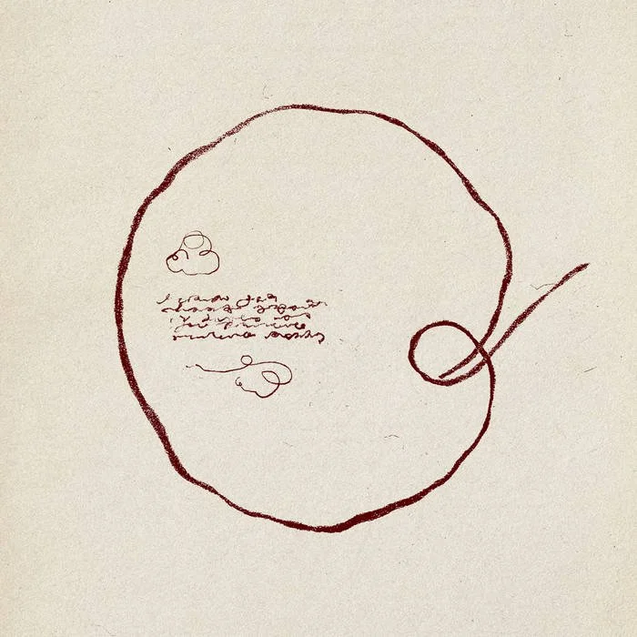 A simple, hand-drawn sketch of a circular object with some scribbled text and a small cloud-like shape inside, along with a line pointing to a smaller circle on the right side.