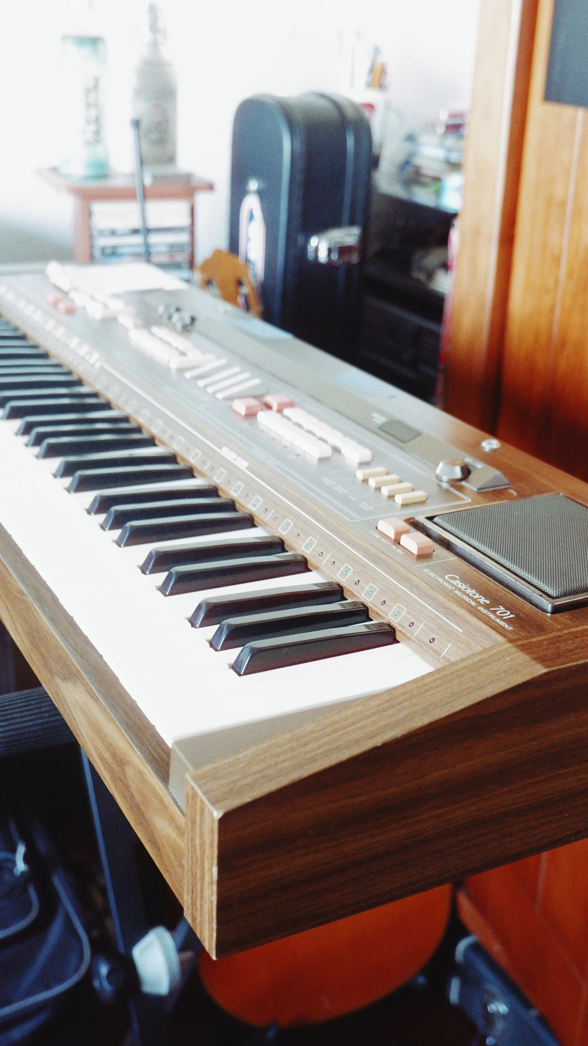An electronic keyboard with a wooden stand in a room with cluttered background.