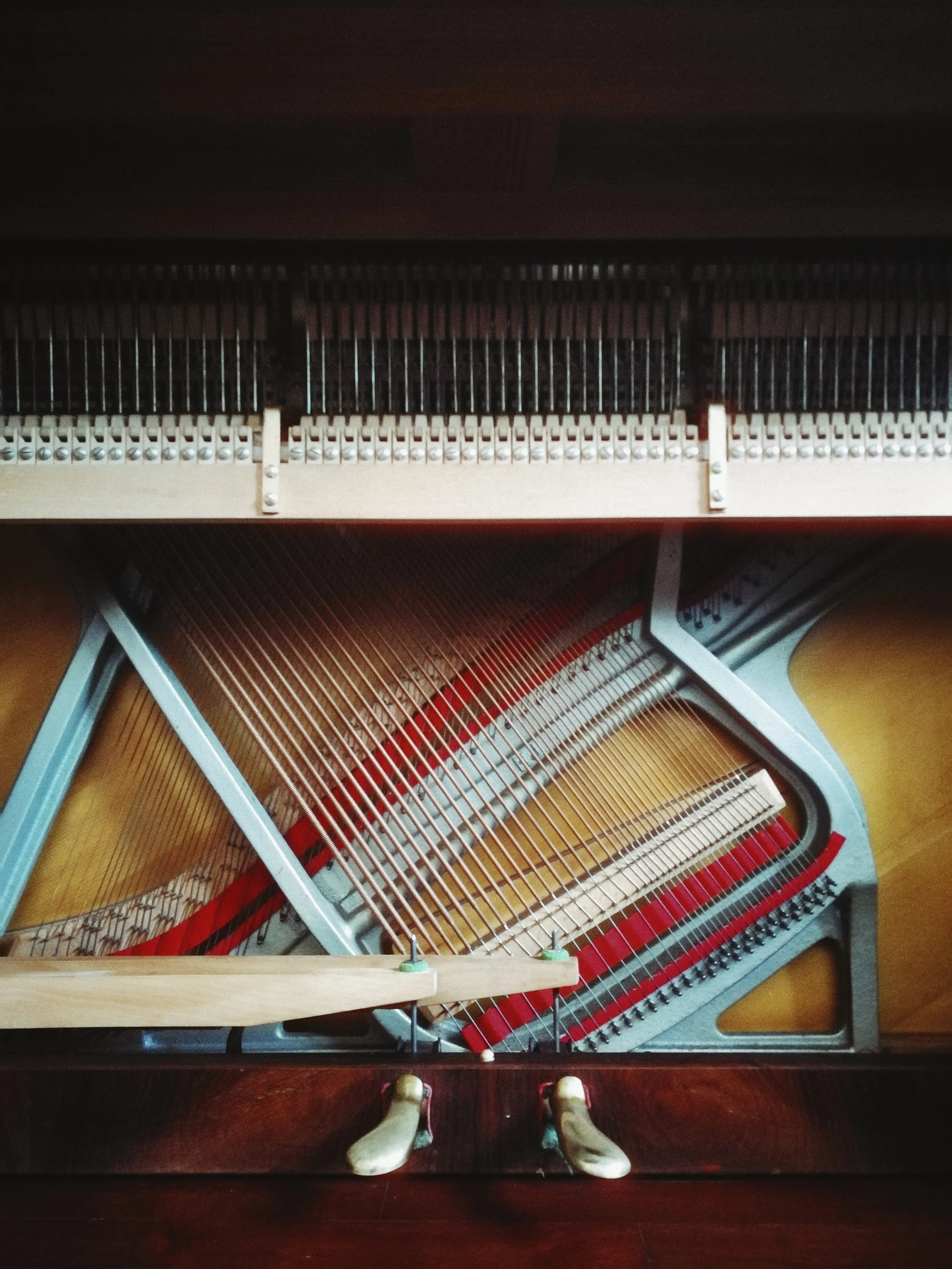 View from above of the inside of a piano showing its strings, hammers, and frame, with a person's feet at the bottom.