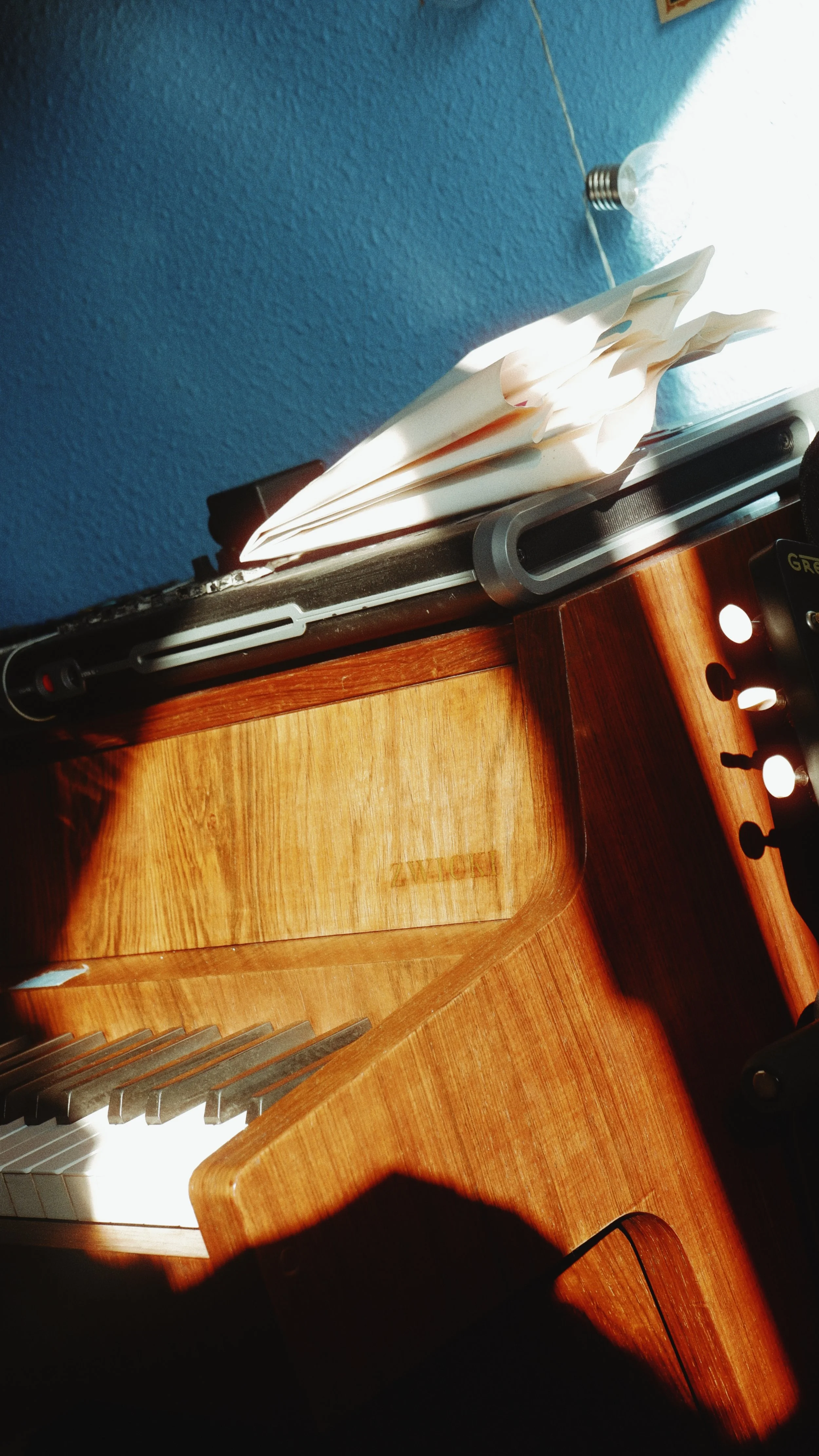 A wooden piano with a sheet of music on top, next to a window with bright light shining through.