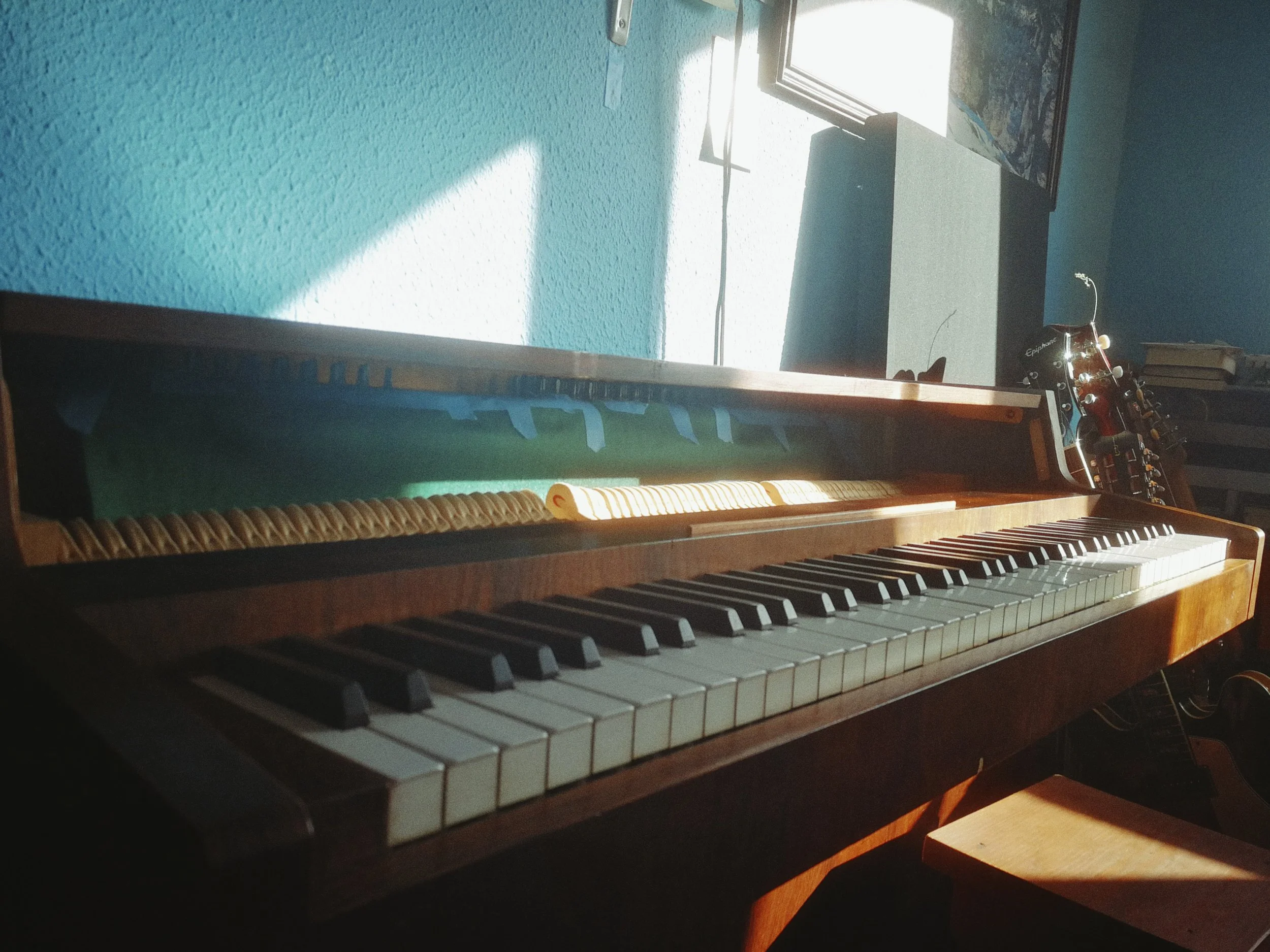 A close-up view of a wooden piano keyboard in a room with a blue wall and a window allowing sunlight to stream in.