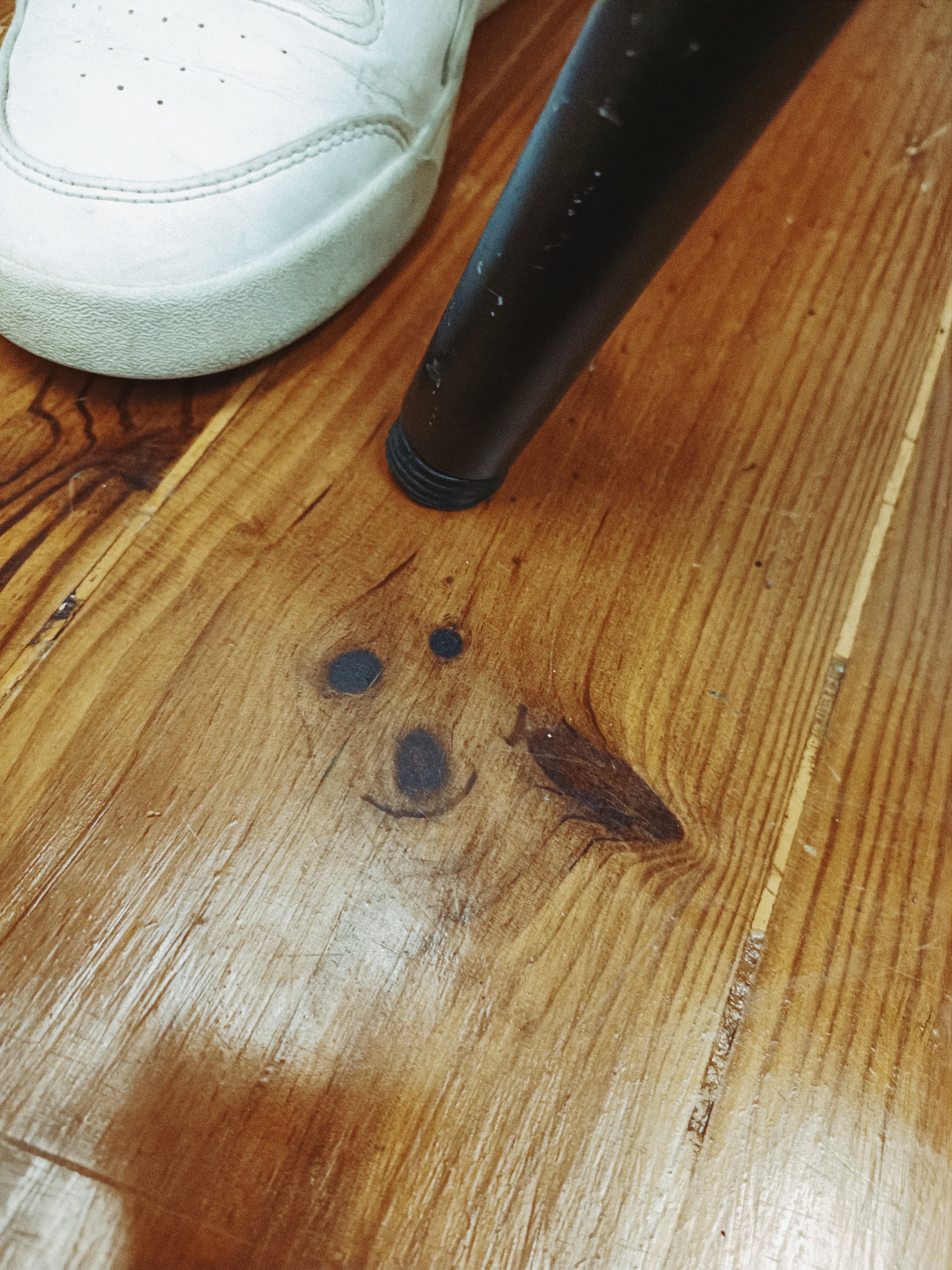 Close-up photo of a white sneaker shoe and a black marker pen on a wooden surface.