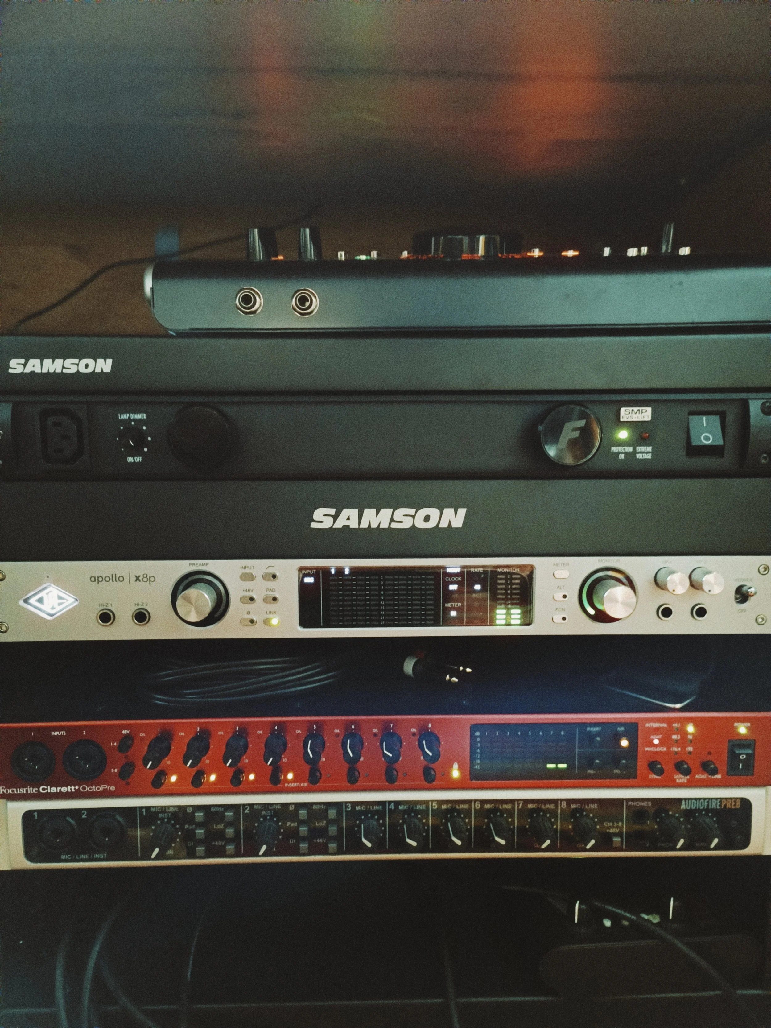 A music studio setup with multiple electronic audio equipment, including a SAMSON amplifier and other audio processing units.