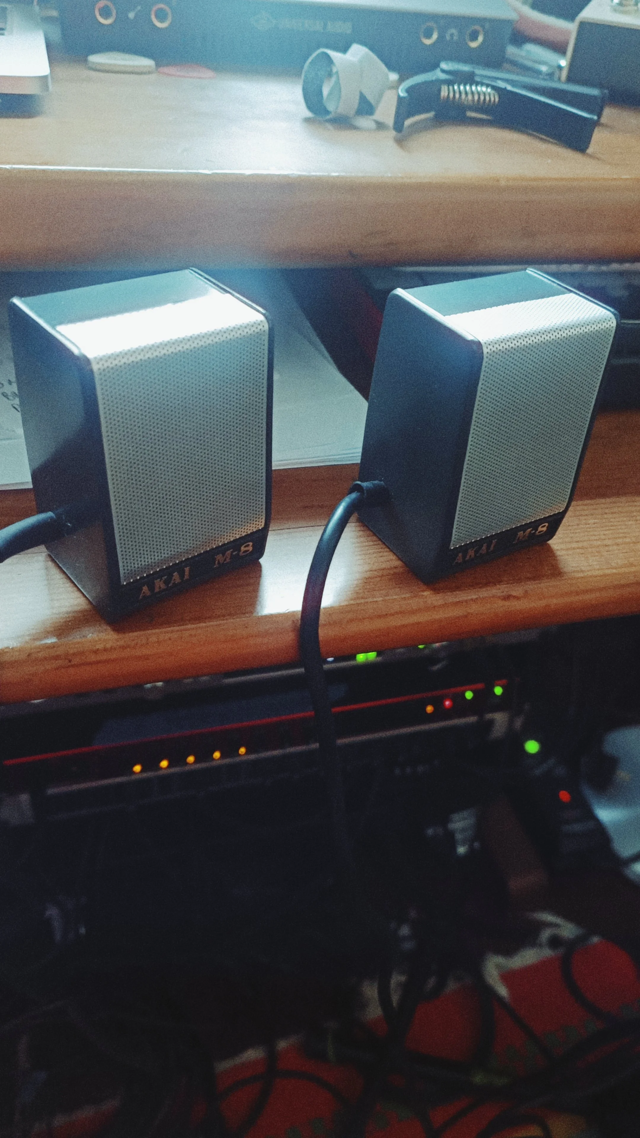 Two small computer speakers with black and silver design connected to cables on a wooden desk.