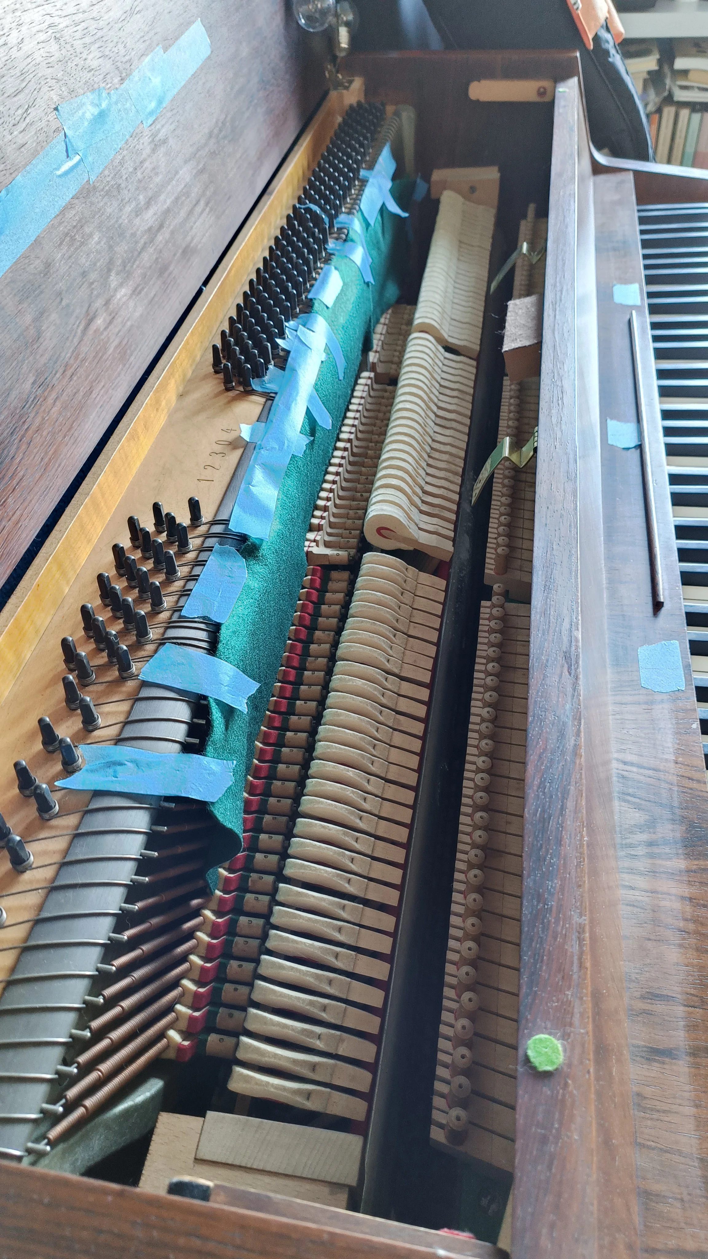 Inside view of an upright piano with exposed internal strings, hammers, and tuning pins, showing parts of the action and felt components.