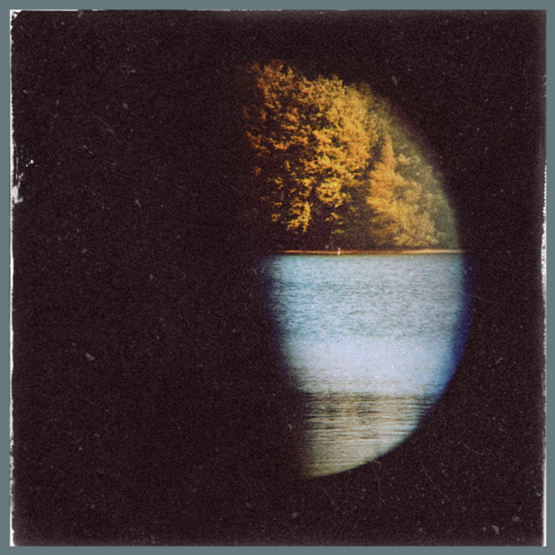 Photo of a view through a tunnel at night, showing a lake and trees with autumn foliage illuminated by warm sunlight.