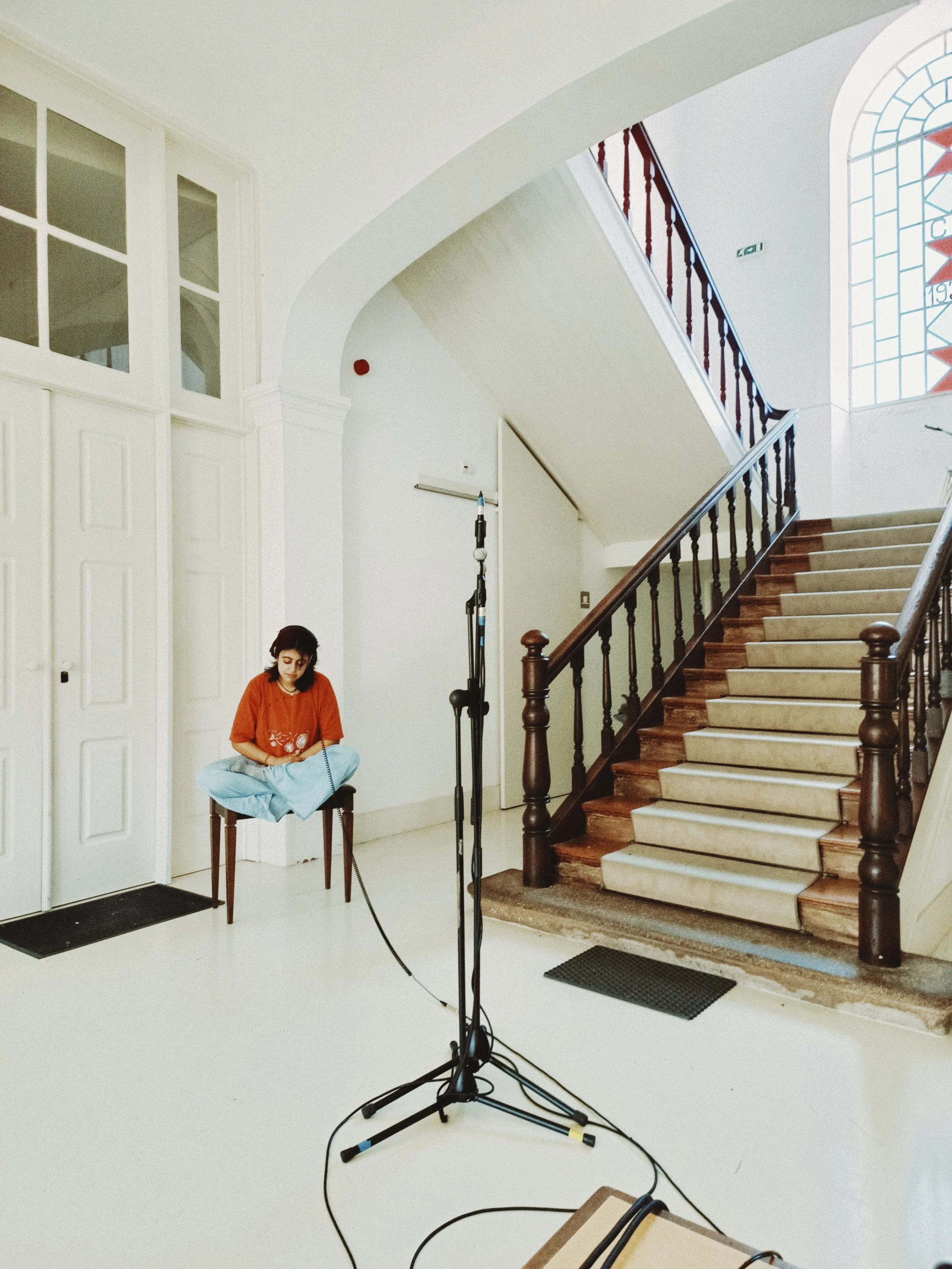 Interior of a building with a staircase and large stained glass window, woman sitting on a chair, professional photography equipment setup.