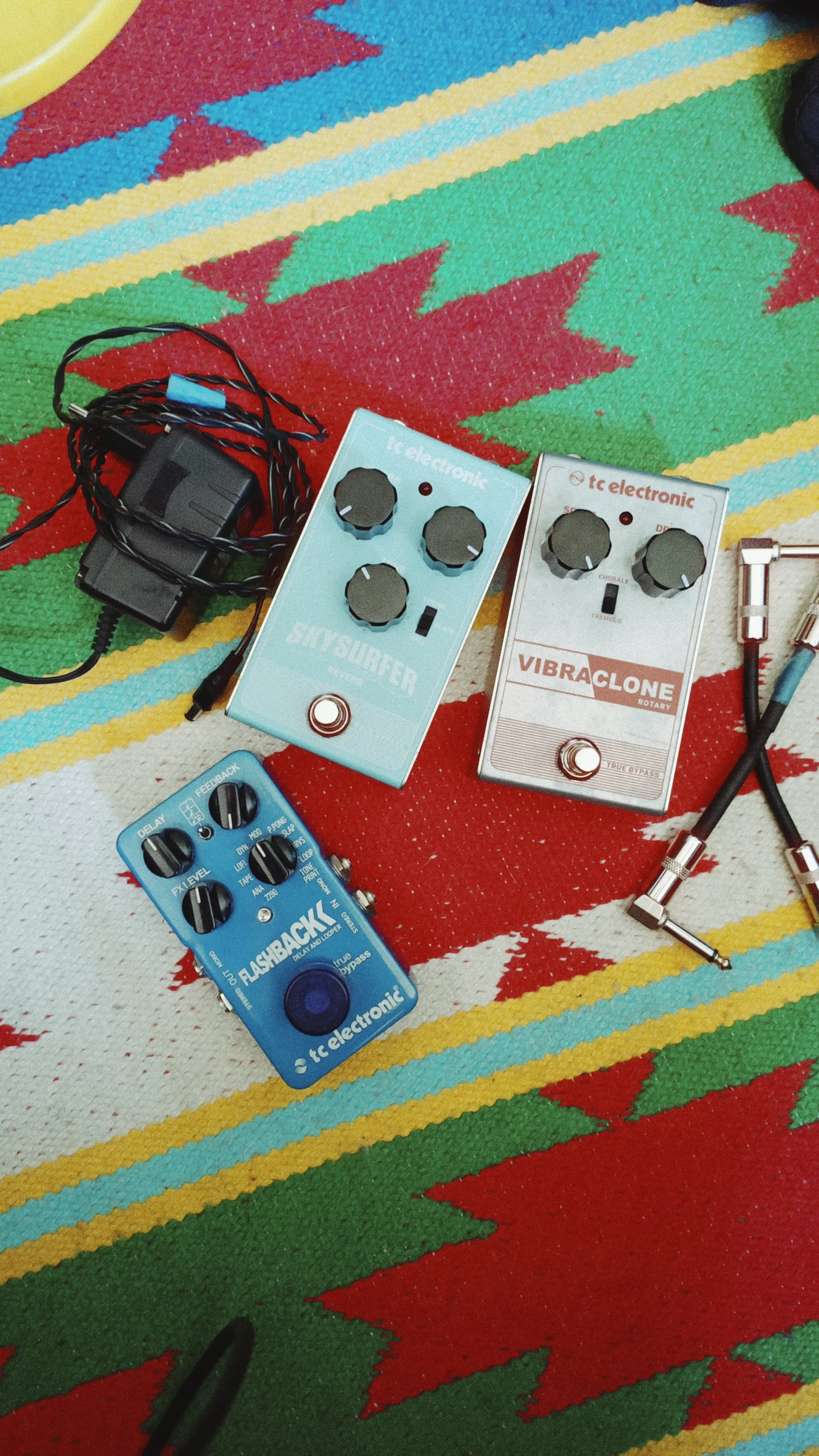 Electric guitar effect pedals on a colorful woven blanket.