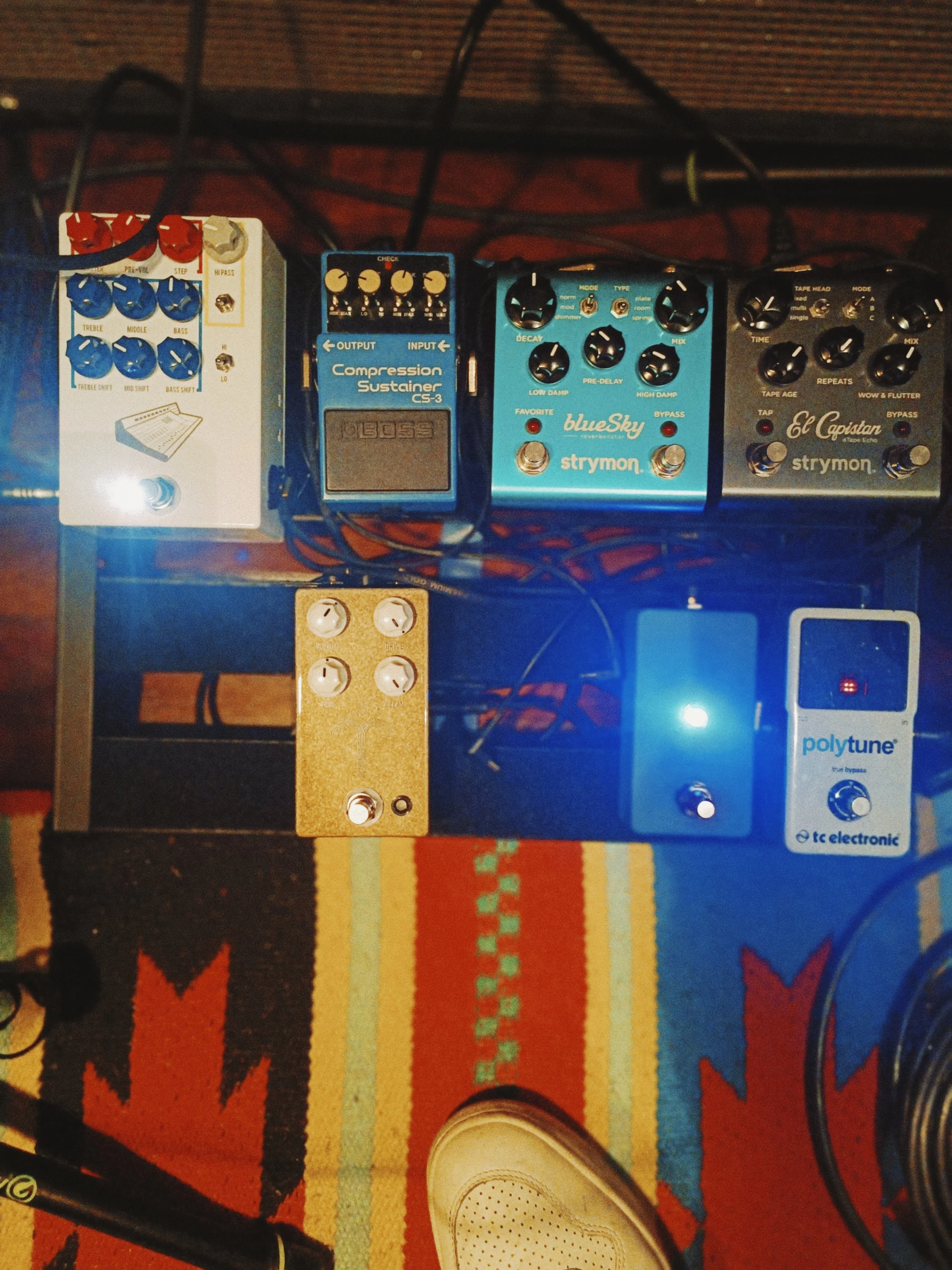 Photo of music pedals on a colorful patterned rug. There are four effect pedals, and various cables connected to them.