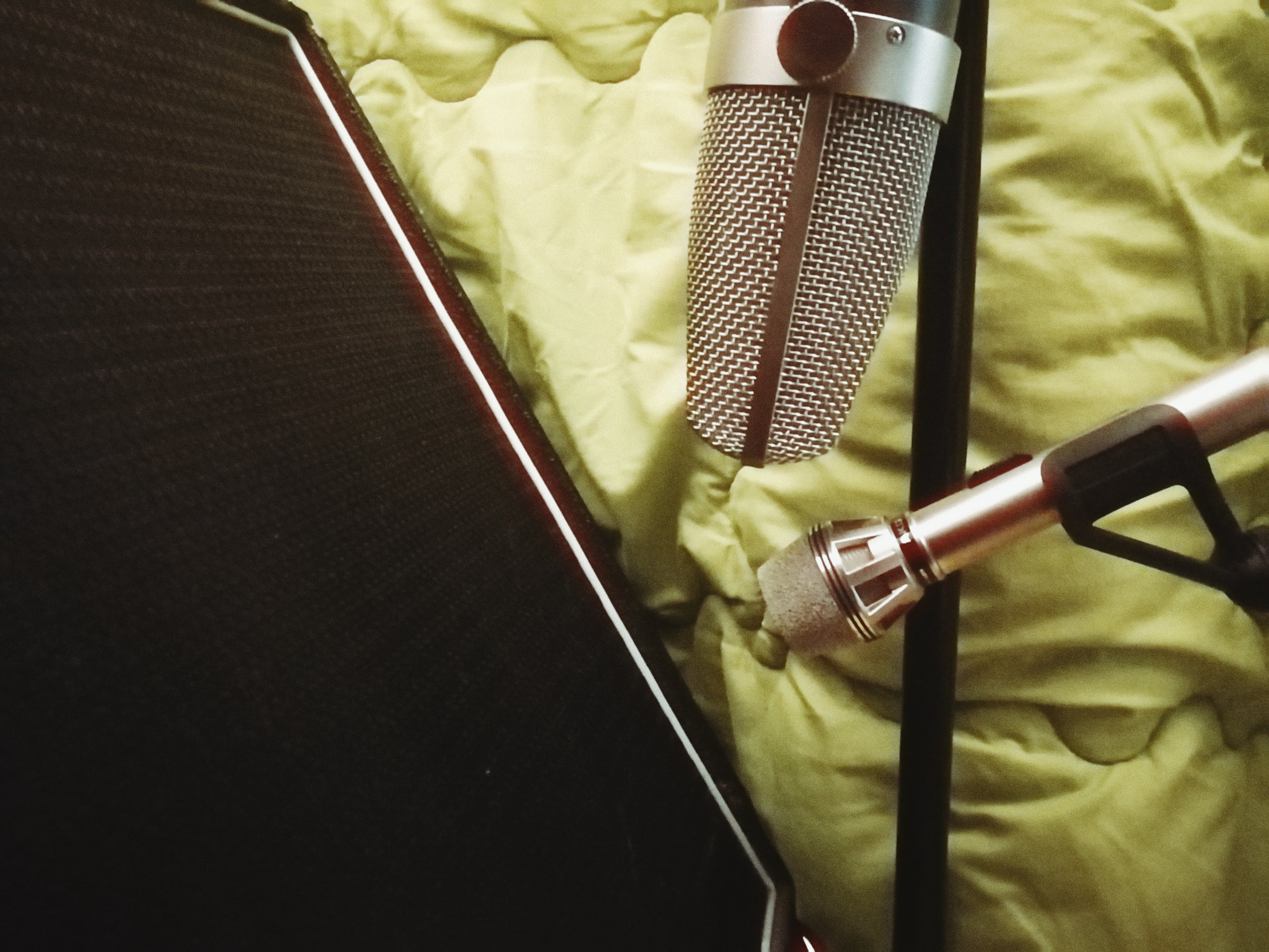 Close-up of a professional condenser microphone resting on a lime green crinkled fabric surface, with a black stand partially visible.