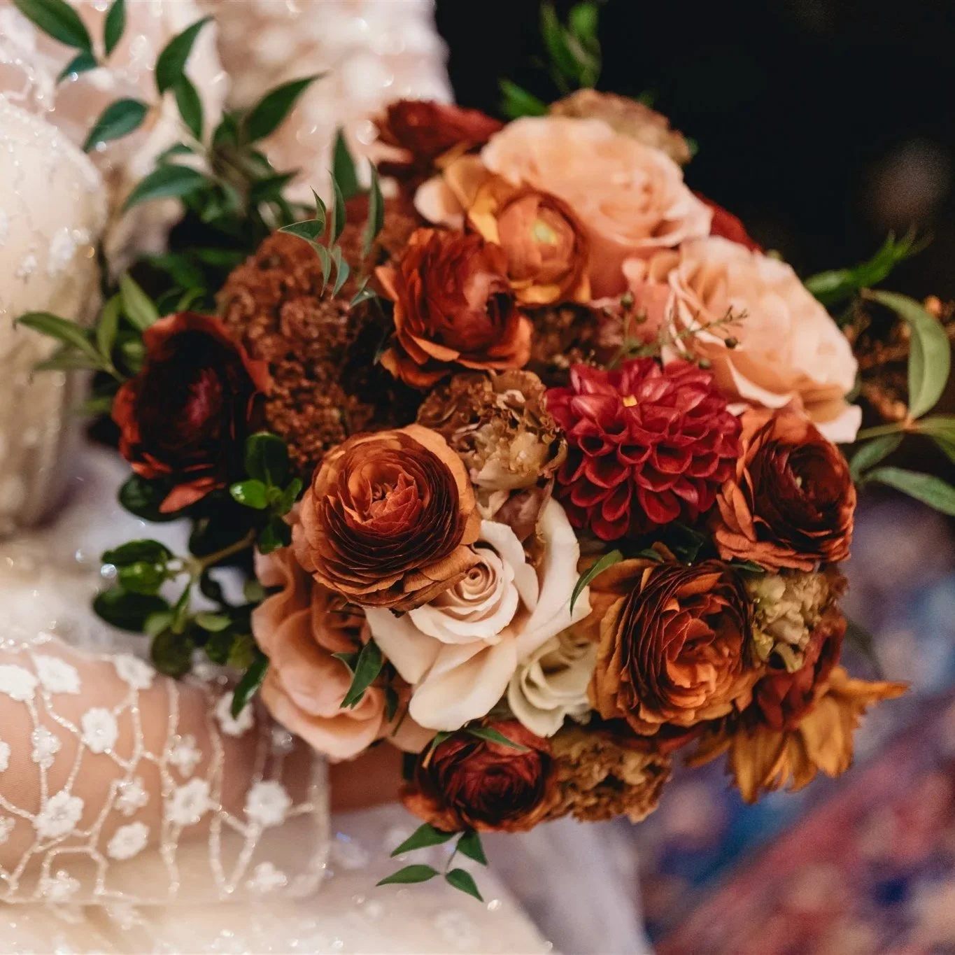 Close-up of a bouquet of dried and fresh flowers, including roses and dahlias, with green leaves, made for a special occasion.