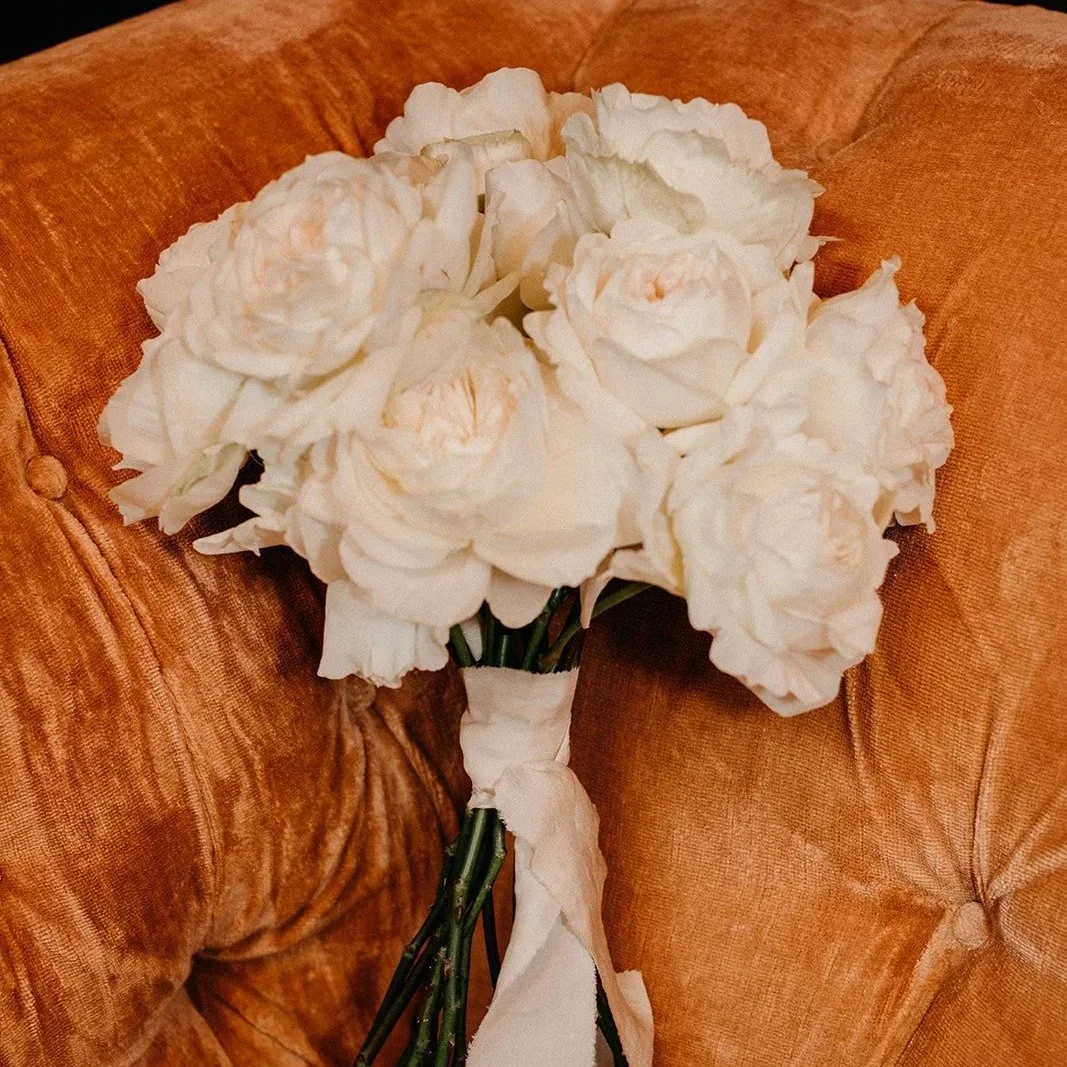 A bouquet of white flowers resting on a tufted, orange velvet couch.
