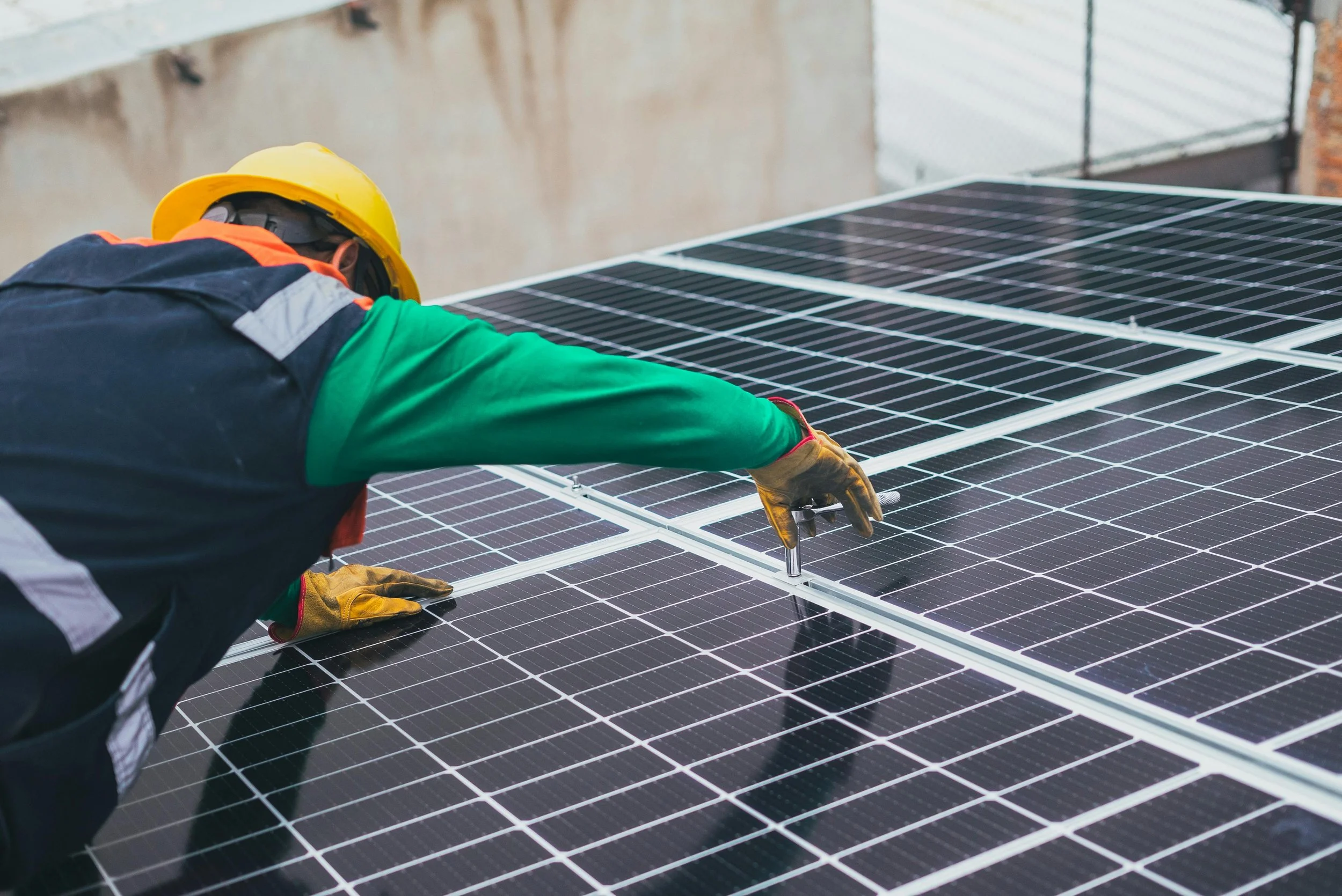 Worker installing or repairing solar panels on a roof, wearing a yellow helmet and gloves.