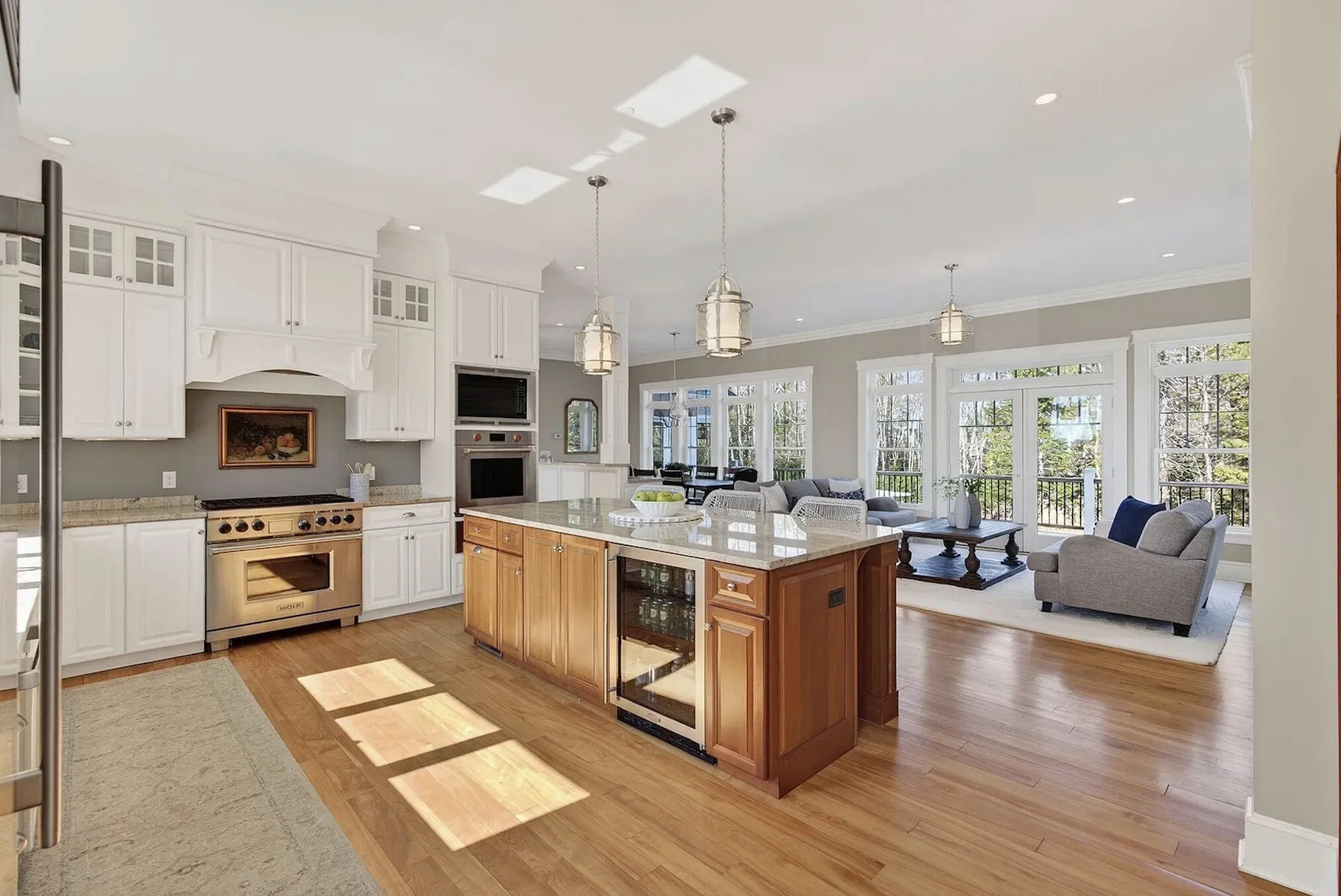 Bright open kitchen and living room with white cabinets, a wooden island, large windows, gray walls, and a cozy seating area.