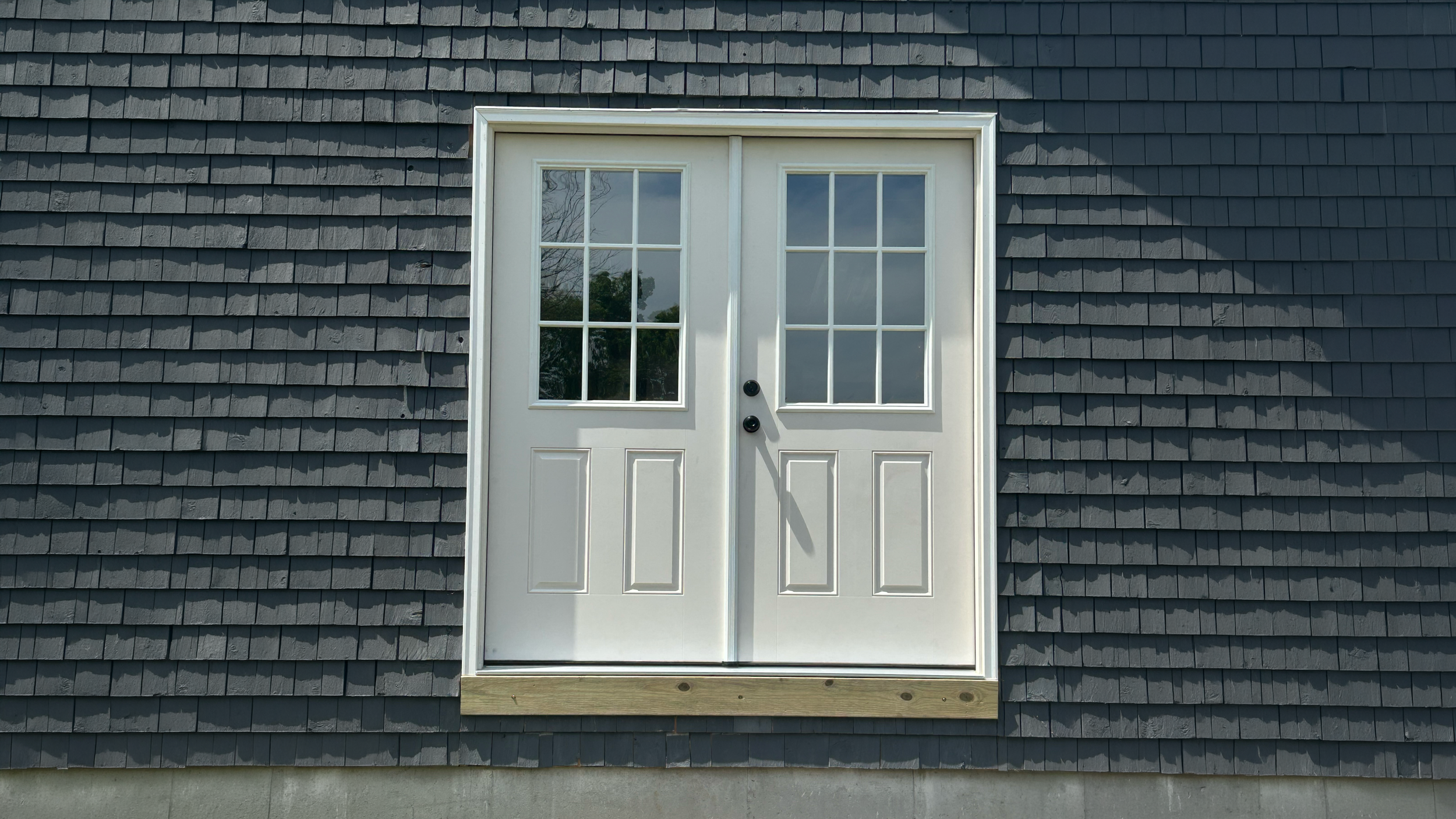 A set of double doors with glass panels on a gray shingled exterior wall.