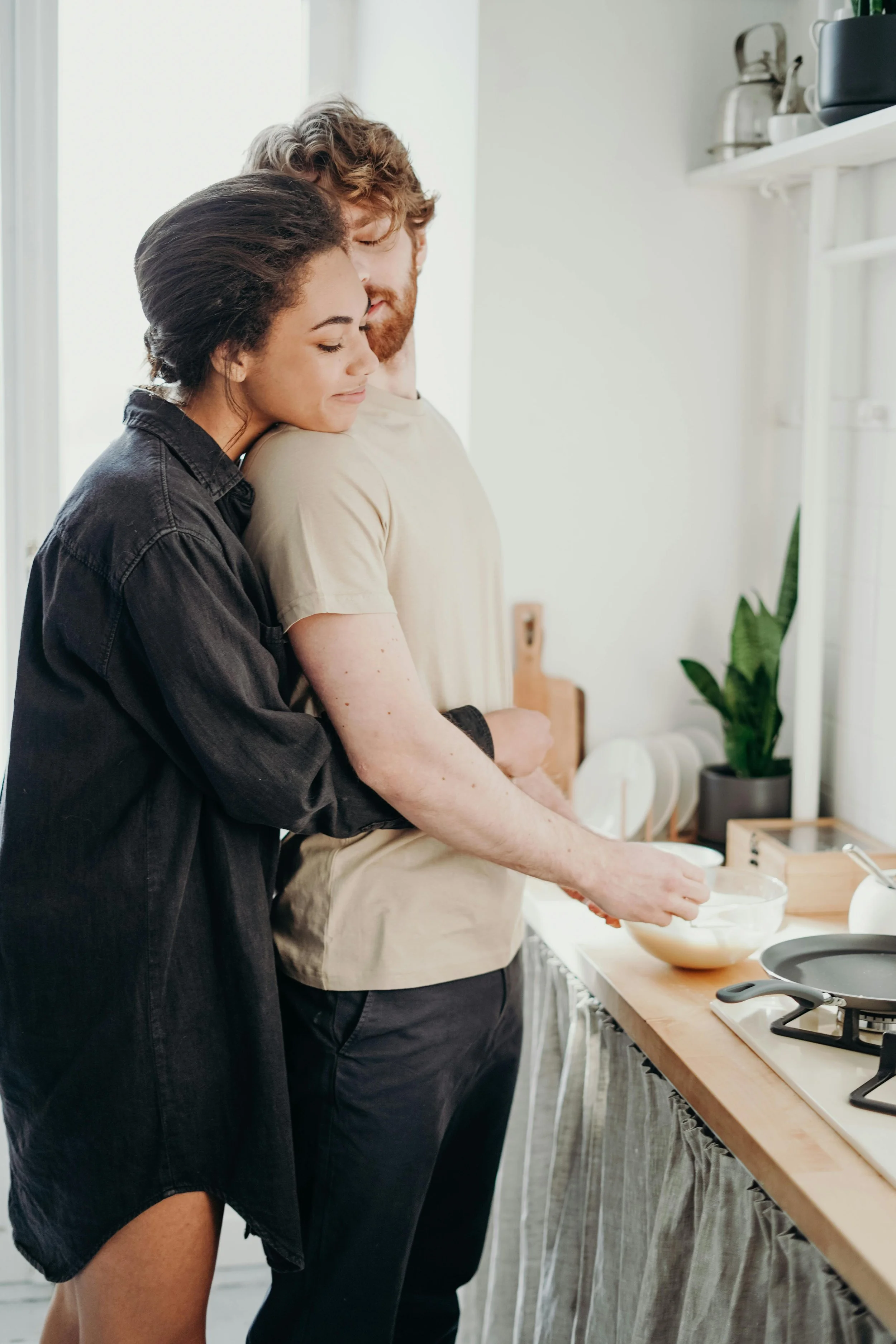 A couple in a cozy kitchen, sharing a tender moment while cooking, with one leaning on the other's shoulder and smiling. Couples therapy and relationship counseling for Washington State partners
