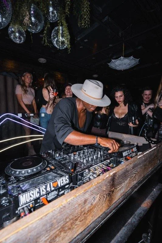 DJ playing music at a nightclub, surrounded by people dancing and socializing.