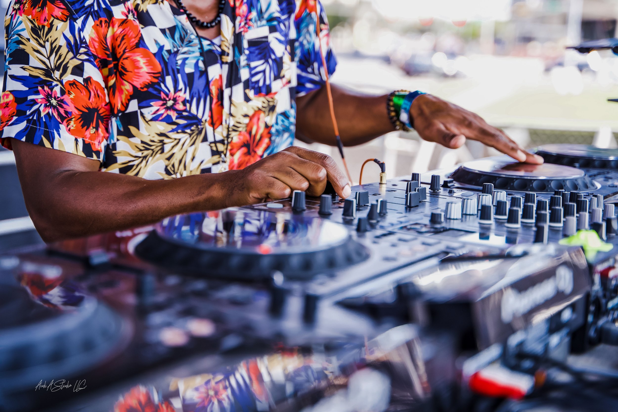 A DJ wearing a colorful floral shirt is mixing music on a DJ controller.