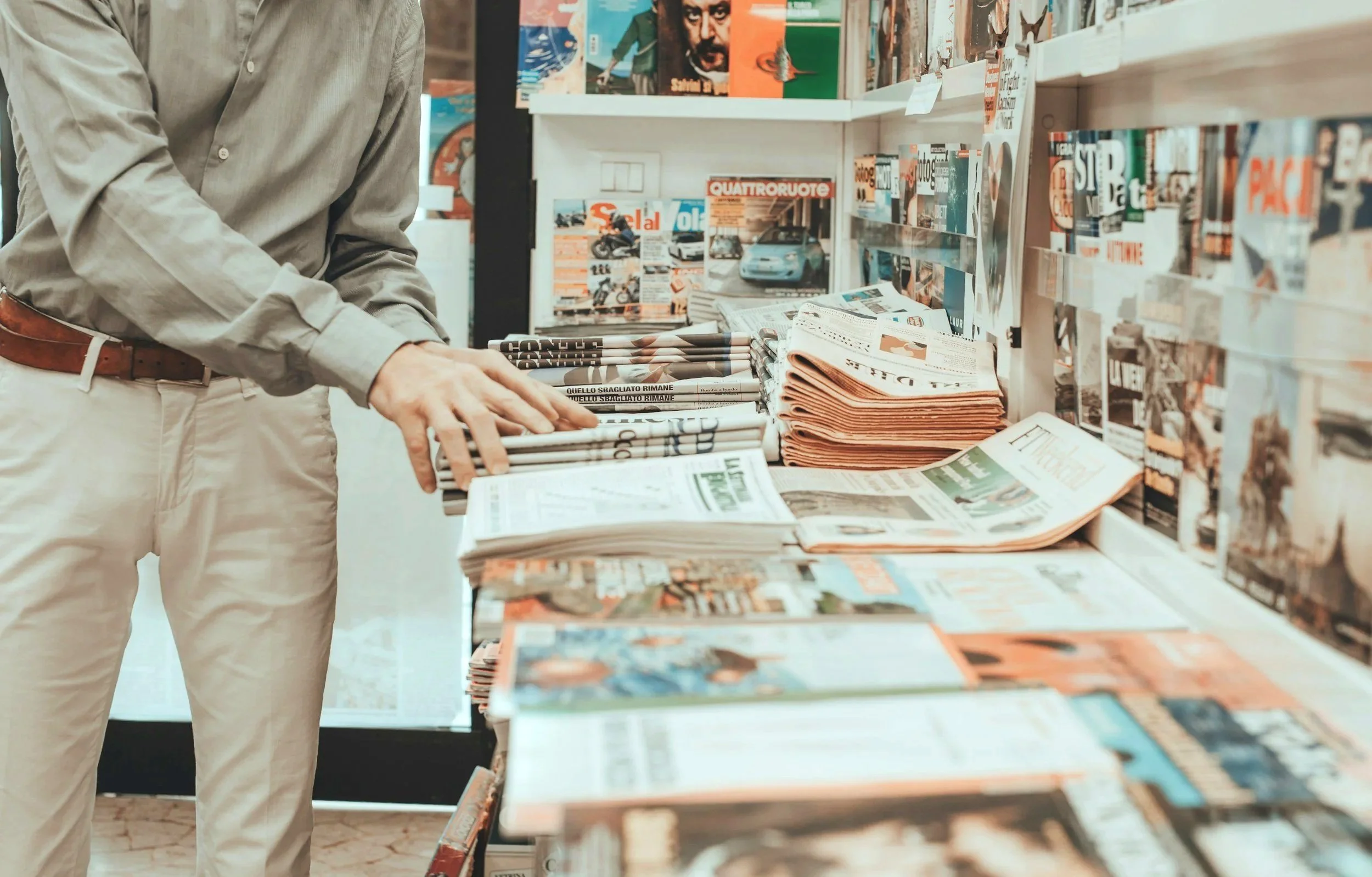 Person browsing newspapers and magazines at a traditional newsstand.