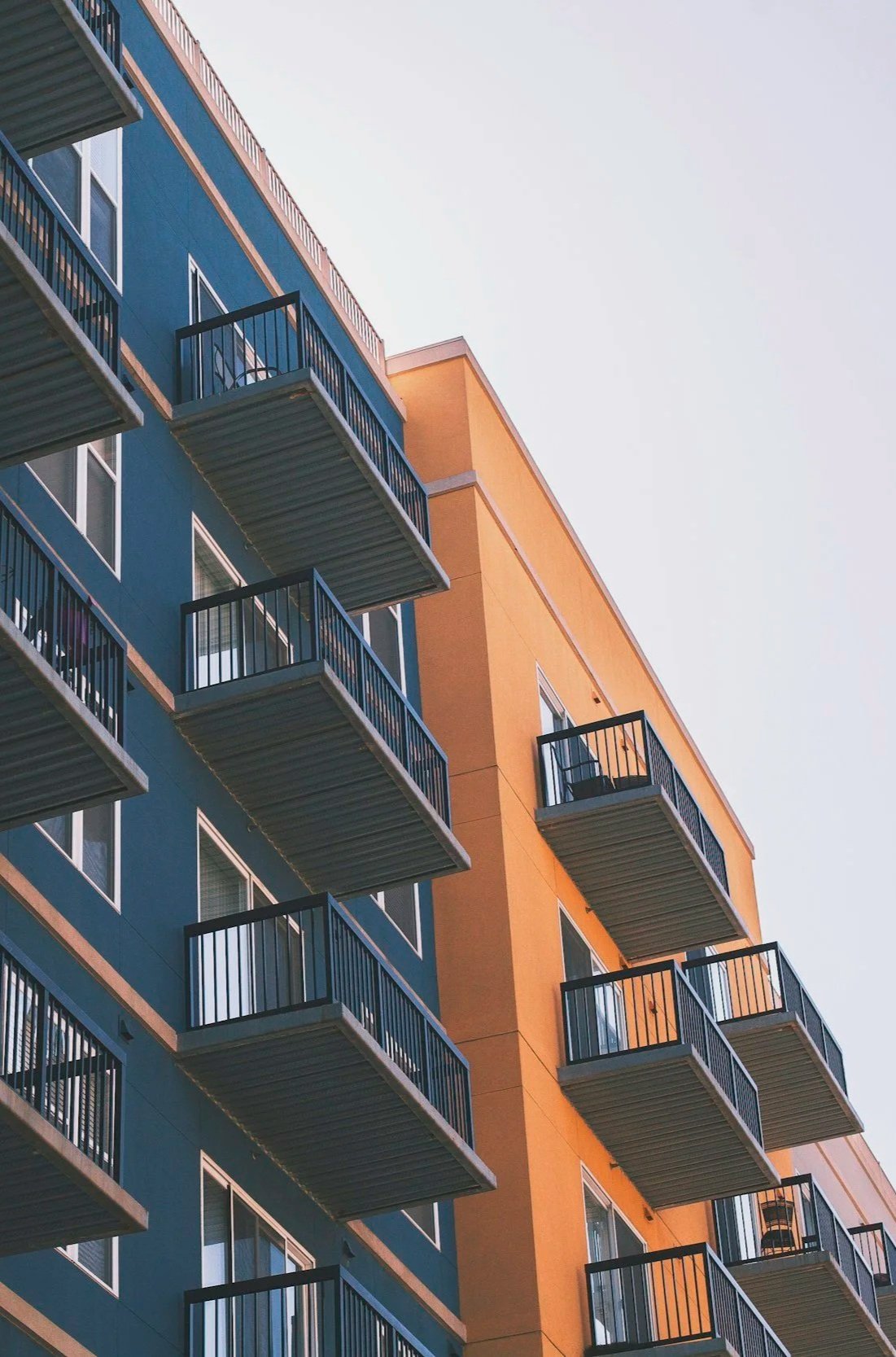 Multiple balconies on a modern apartment building, with one chair visible on a balcony, painted in blue and orange colors.