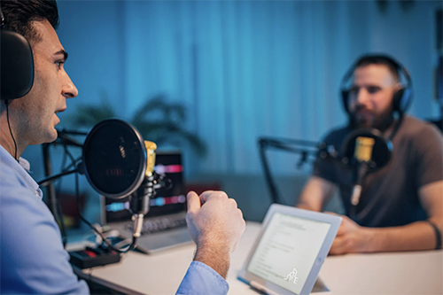 Two men with headsets recording a podcast at a studio with microphones and a tablet.