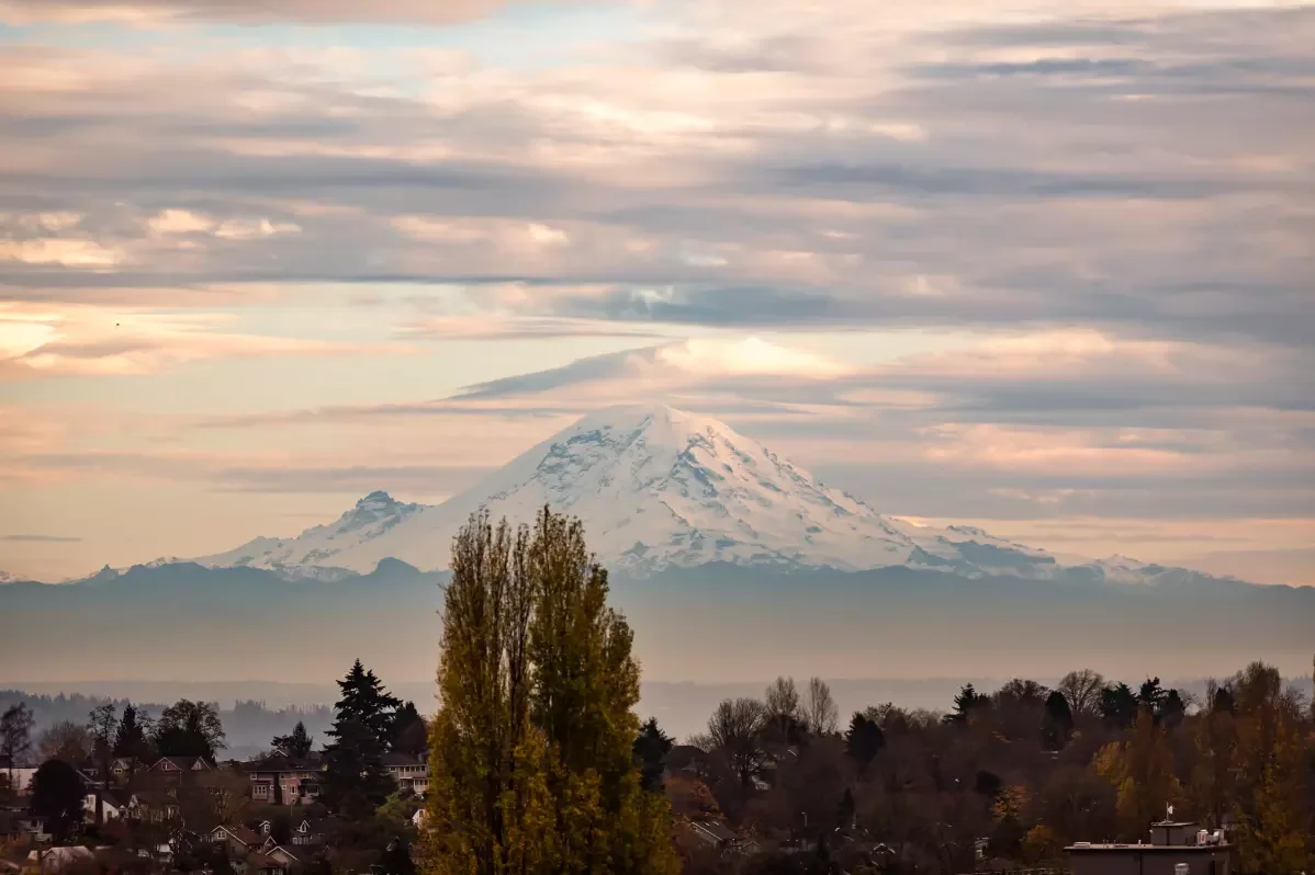 Snow-capped mountain in the distance with a town and trees in the foreground.