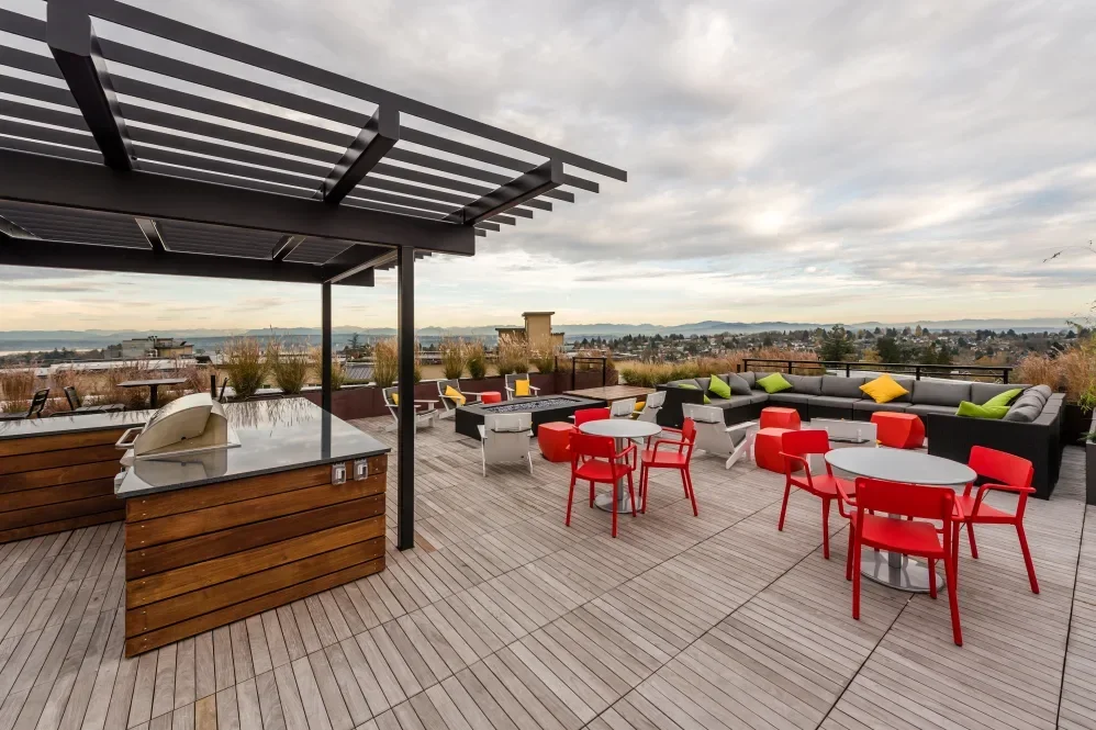 Rooftop terrace with outdoor seating, tables, colorful chairs, a grill counter, and a city view with mountains in the background.