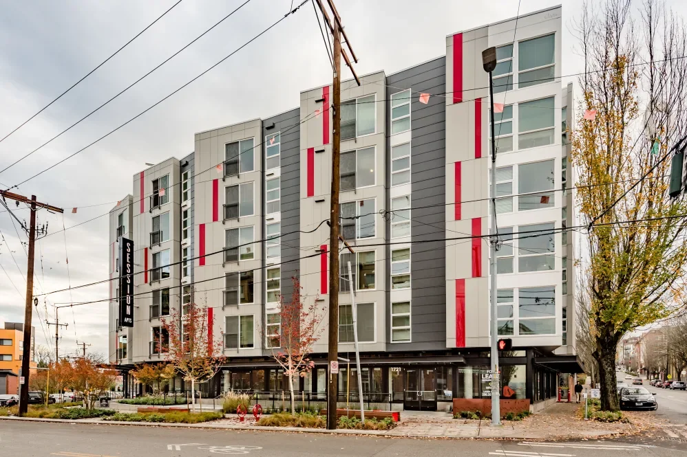 Modern multi-story apartment building on a city street with trees, power lines, and a traffic signal