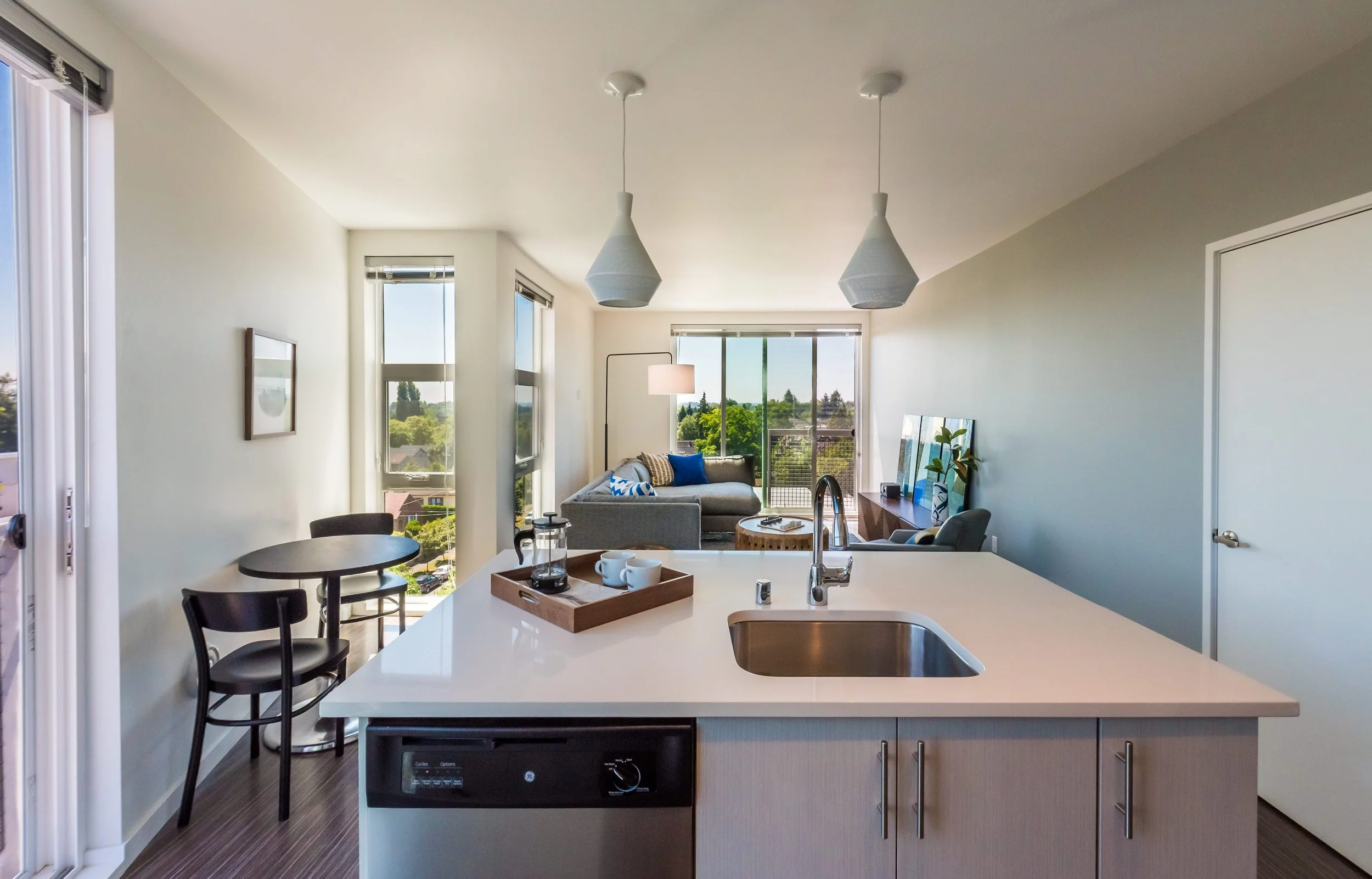 Modern apartment interior with open kitchen and living area, large windows, and white walls.