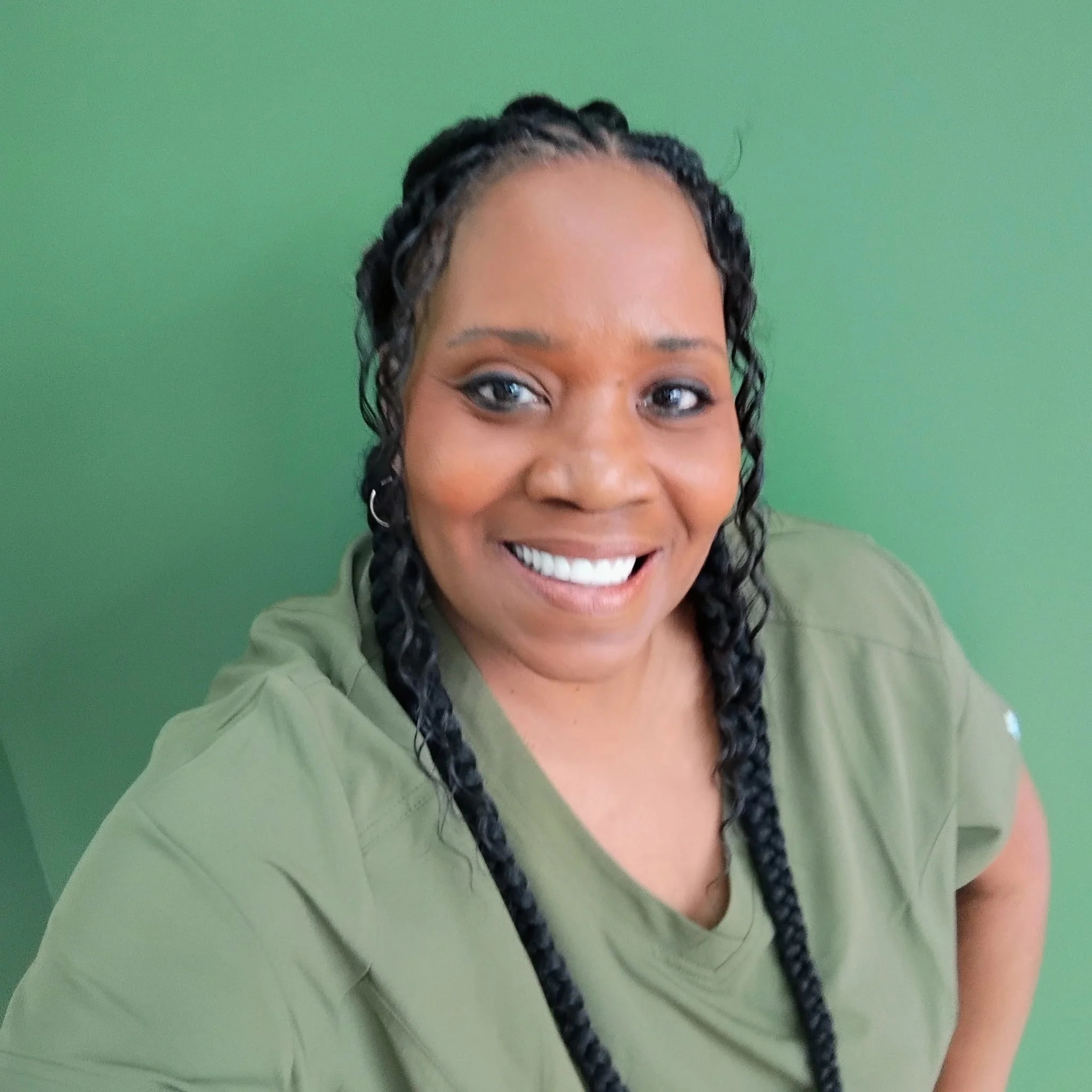 Close-up of a smiling woman with braided hair, wearing a green shirt, against a green background.
