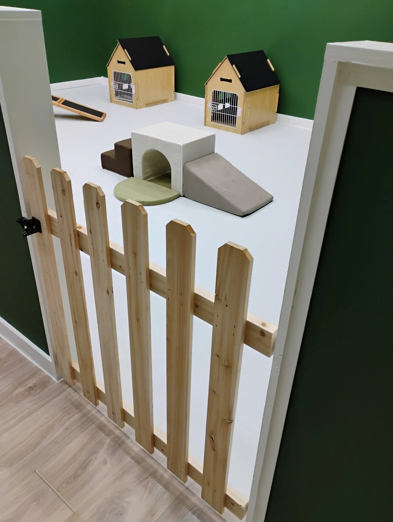 A fenced-off play area with two small wooden pet houses and various pet accessories inside.