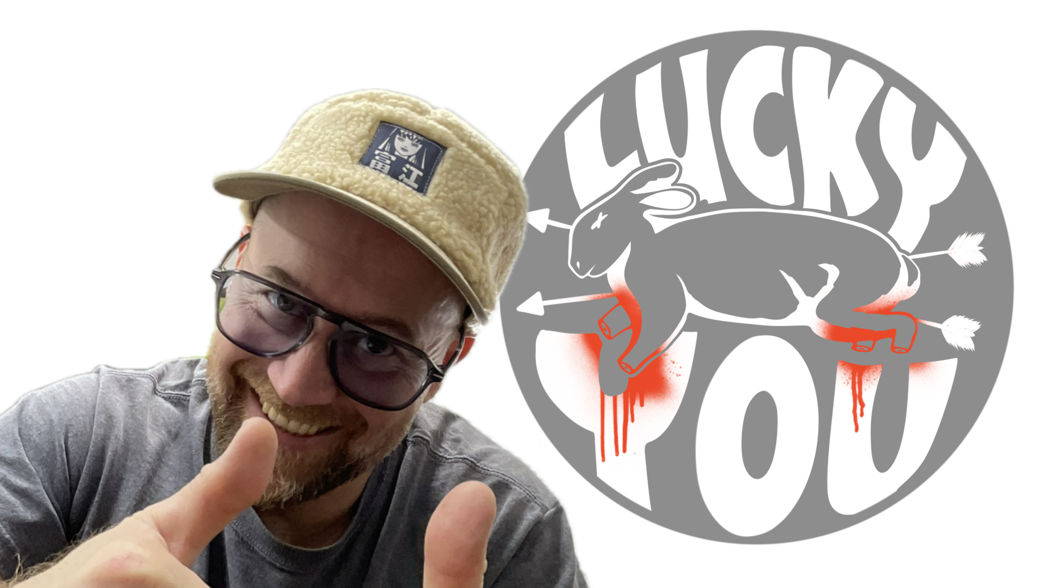 A smiling man with glasses wearing a beige cap and gray shirt shows a thumbs-up gesture, standing in front of a large logo featuring a gray rat with red eyes and a red background.