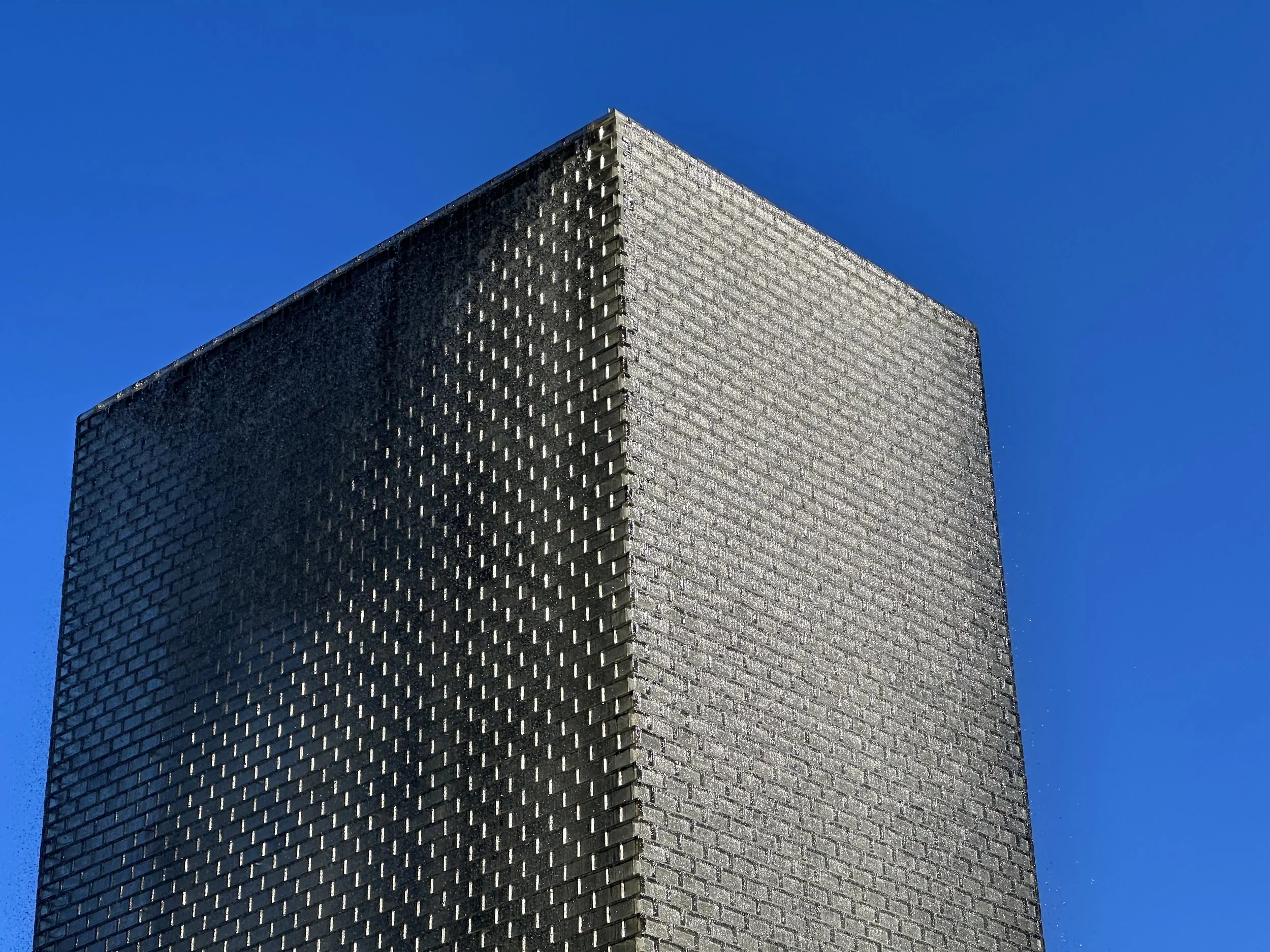 Close-up of a tall building with a glass exterior reflecting sunlight, against a clear blue sky.