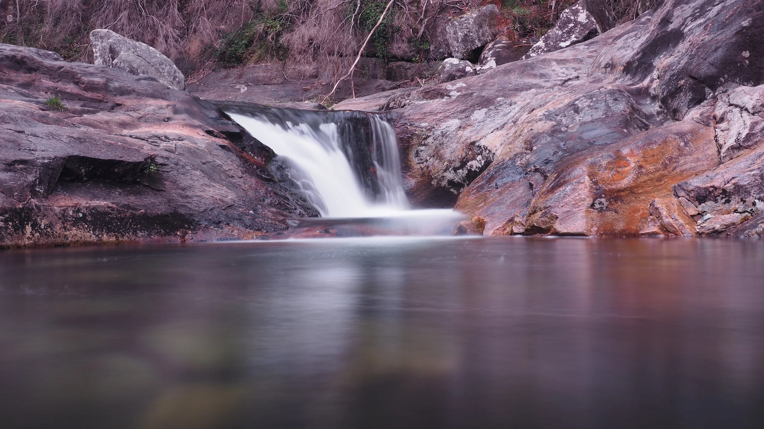 Calm river with a small waterfall flowing over rocks surrounded by trees.