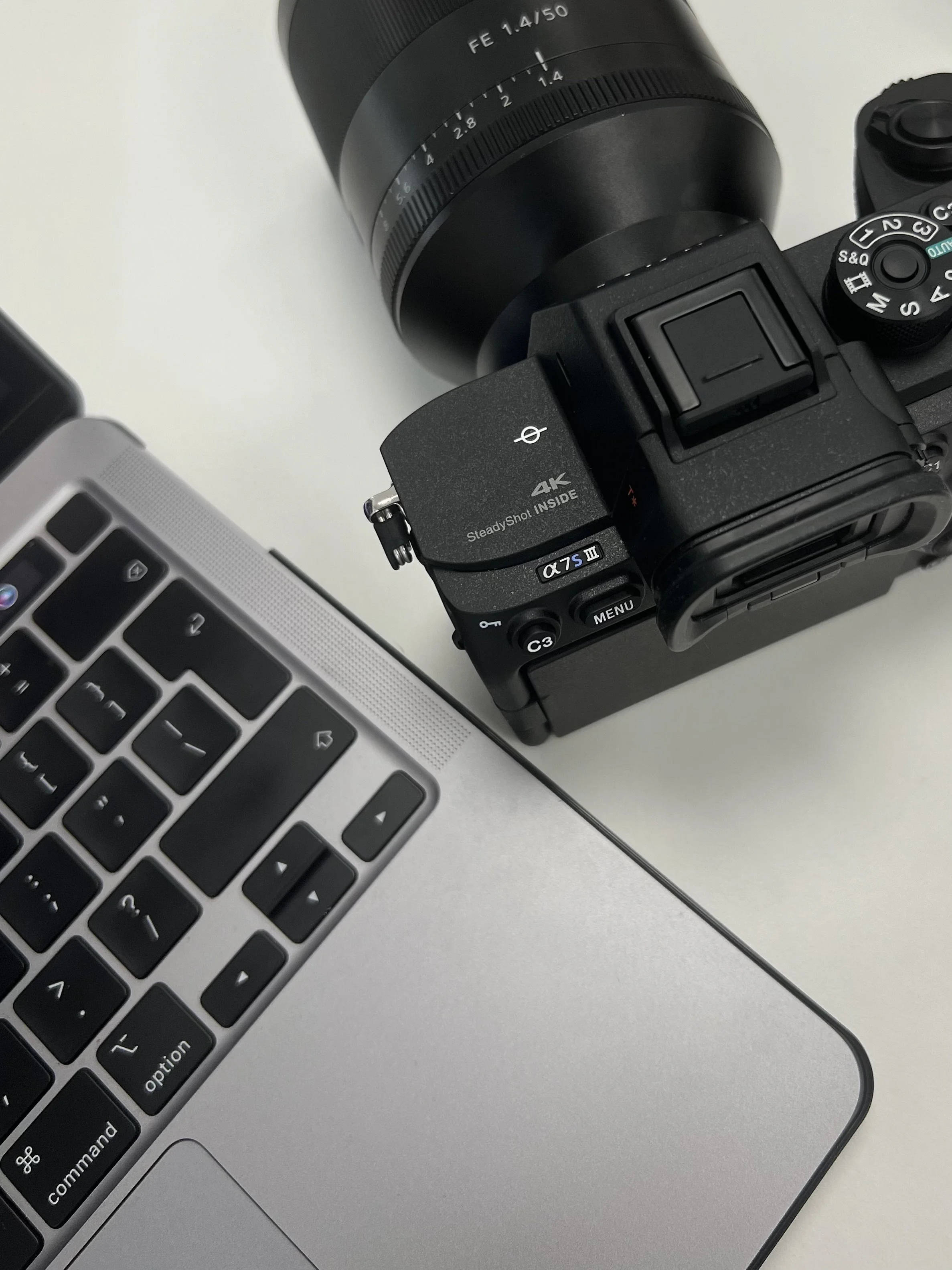 Close-up view of a digital camera with a zoom lens, partially visible laptop keyboard, and a gray surface background.