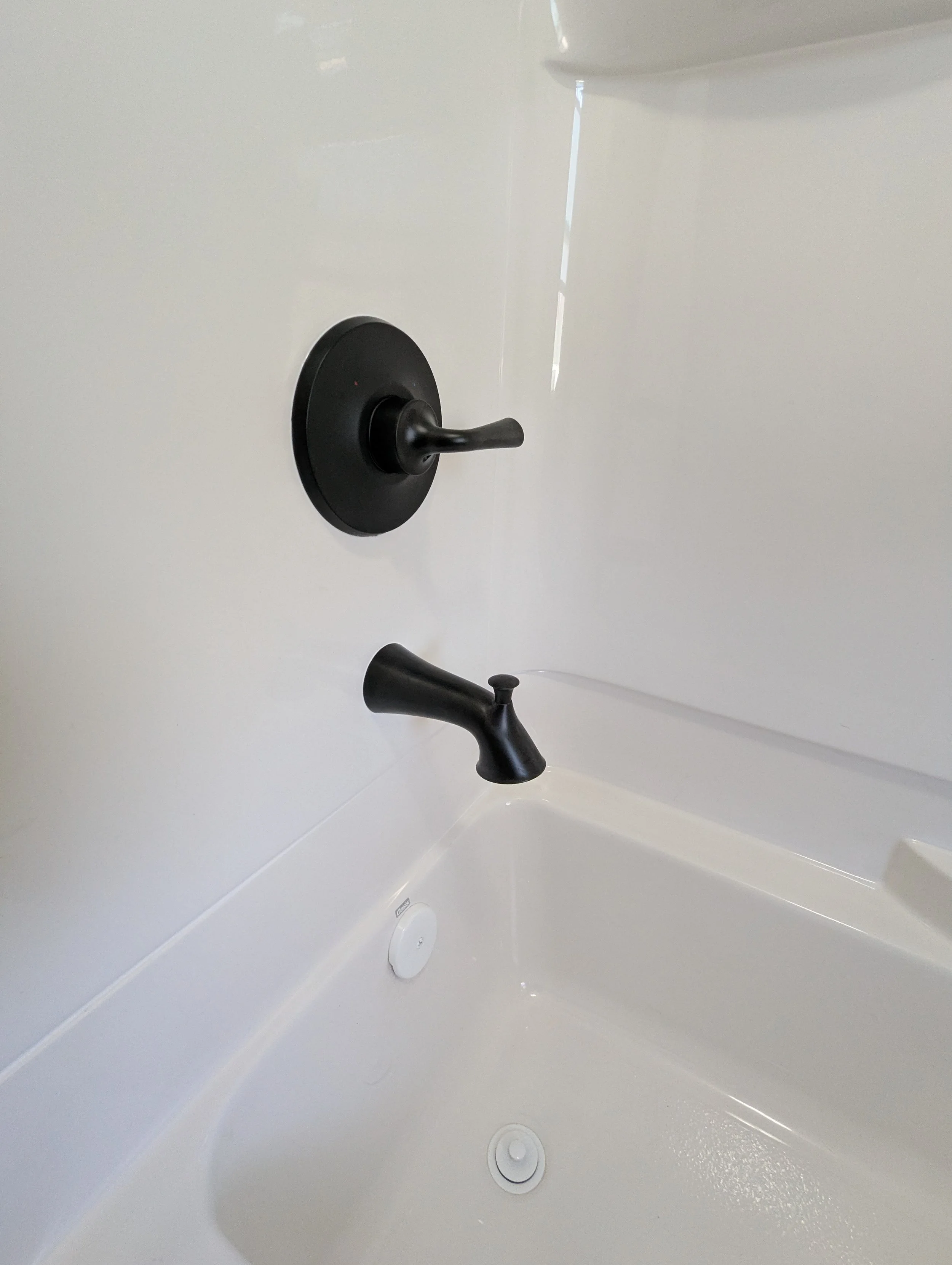 Close-up of a white bathtub with a black faucet and a black shower handle on a white wall.