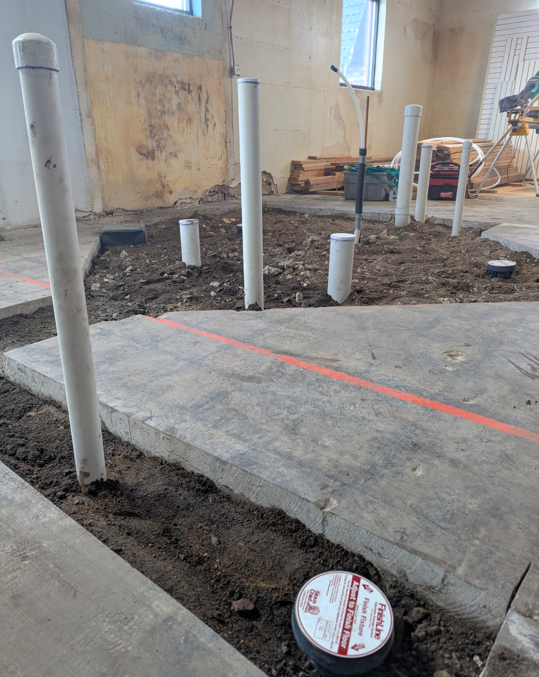 Construction site with exposed pipes and marked areas for flooring installation