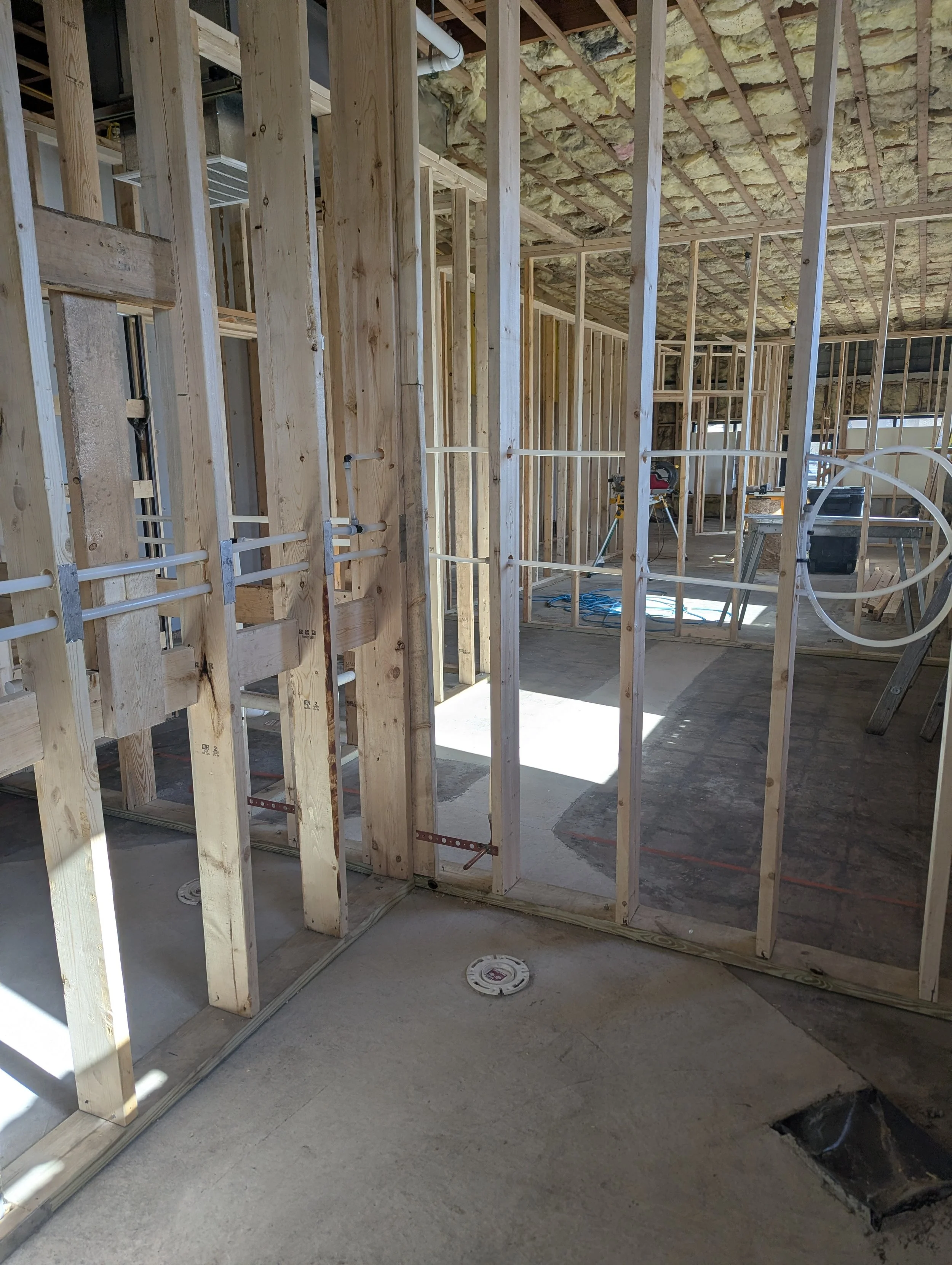 Construction site with wooden framing for interior walls, exposed ceiling insulation, concrete flooring, and various construction tools and materials.